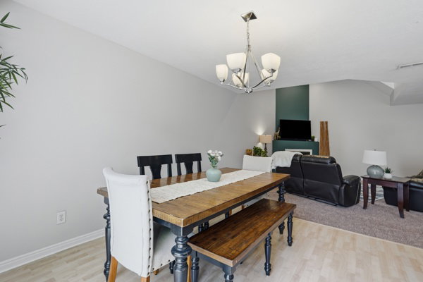 Open-concept dining and living area featuring light wood-finish flooring, a contemporary chandelier, and a focused wall accent with a fireplace surround