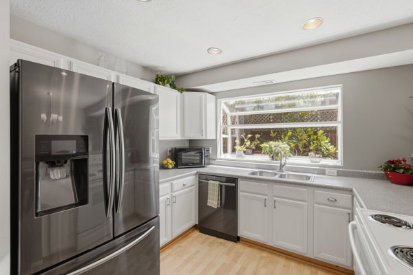 Kitchen featuring a stainless-steel French door refrigerator, white cabinetry, a double basin sink, light-toned wood-finish flooring, and a large garden window