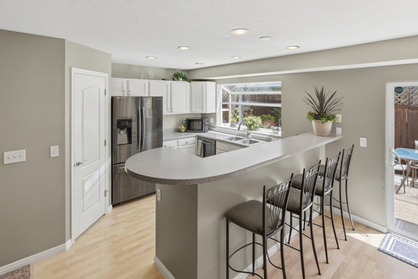 Kitchen featuring an extended breakfast bar, stainless steel refrigerator, white cabinetry, light wood-finish flooring, and recessed lighting