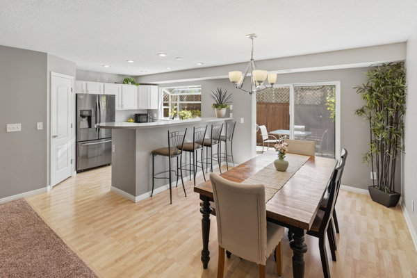 Open-concept living space with light wood-finish flooring, featuring a kitchen with white cabinetry and stainless steel appliances, a breakfast bar with seating, and a dining area