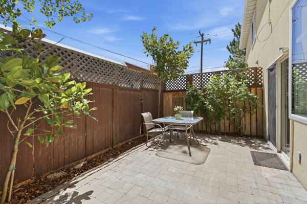 Private outdoor patio featuring paver flooring, wood fencing with lattice accents, and mature plantings