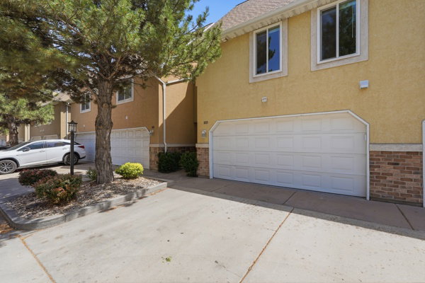 Exterior featuring stucco siding, white-trimmed windows, a two-car garage, and a brick foundation accent