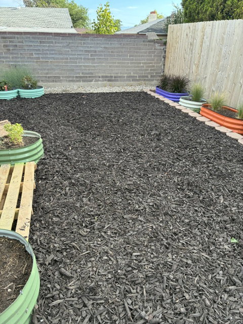 Backyard area featuring dark-toned wood chip ground cover
