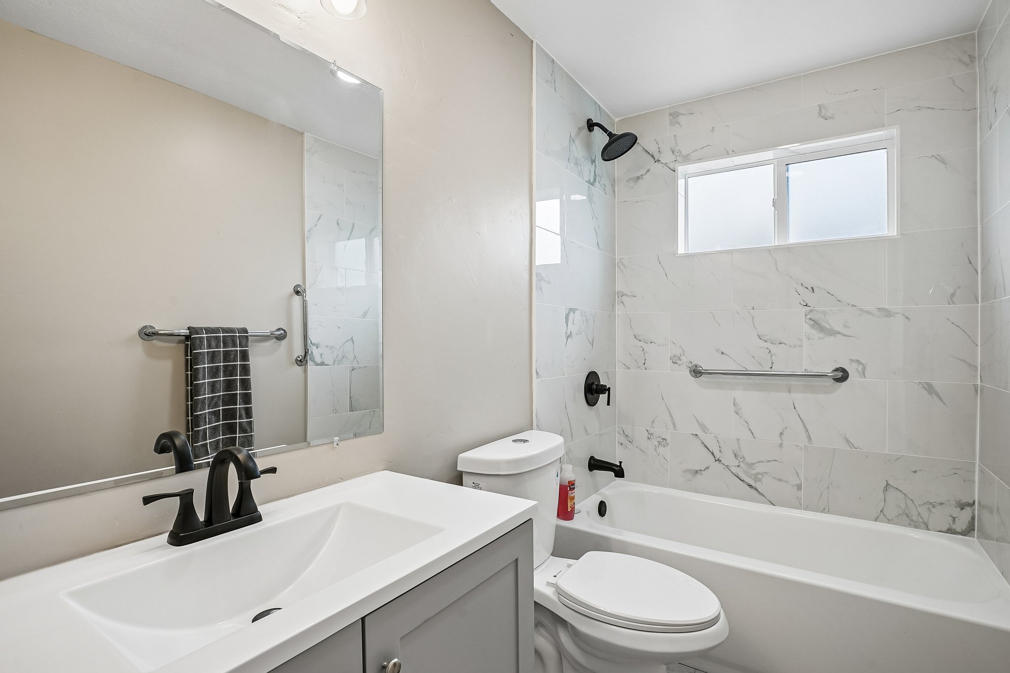Bathroom featuring a white bathtub, white vanity with integrated sink, matte black fixtures, and marble-look wall tiling
