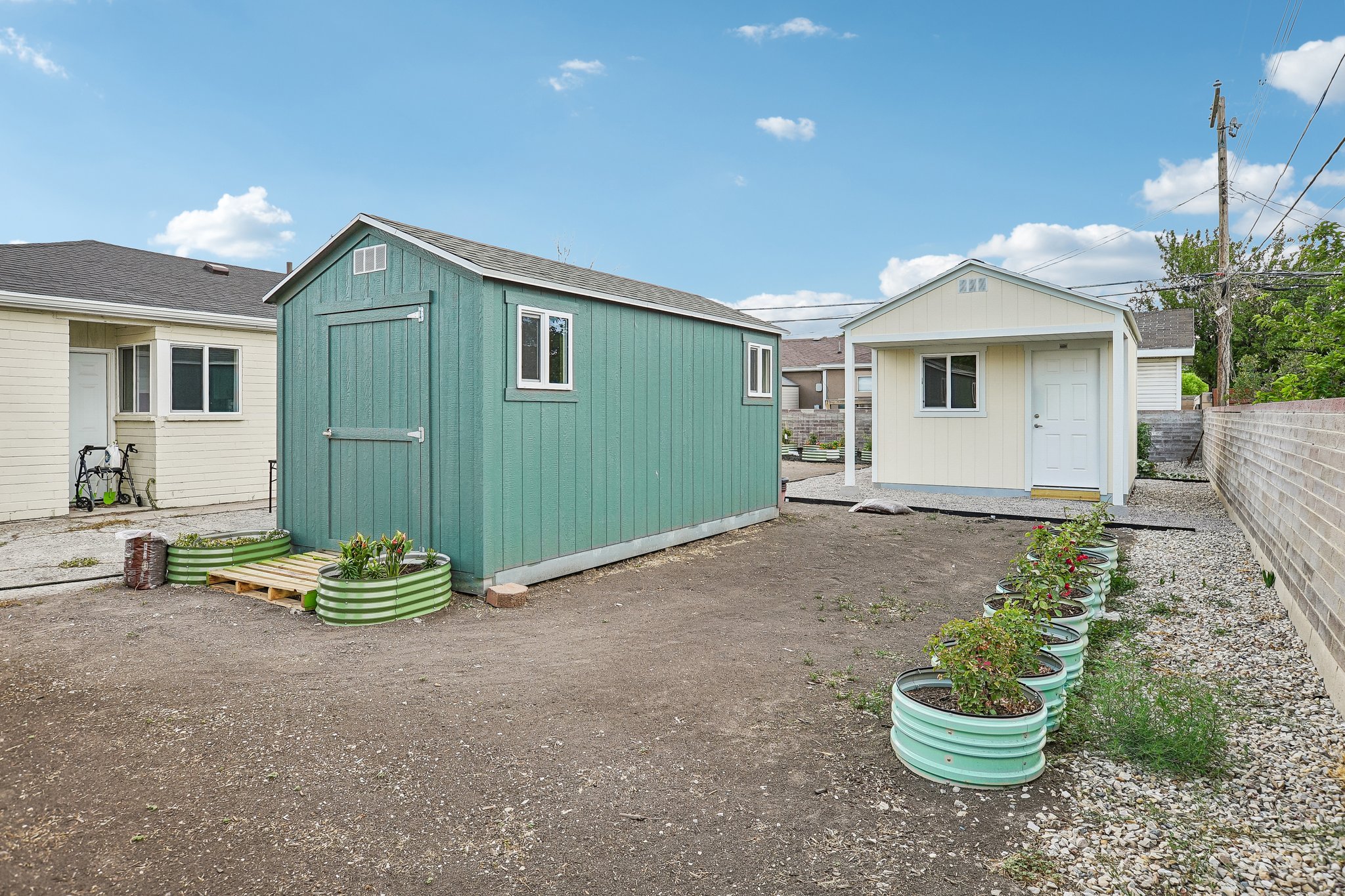 Spacious backyard featuring two distinct outbuildings, a brick perimeter wall, and several corrugated metal planters