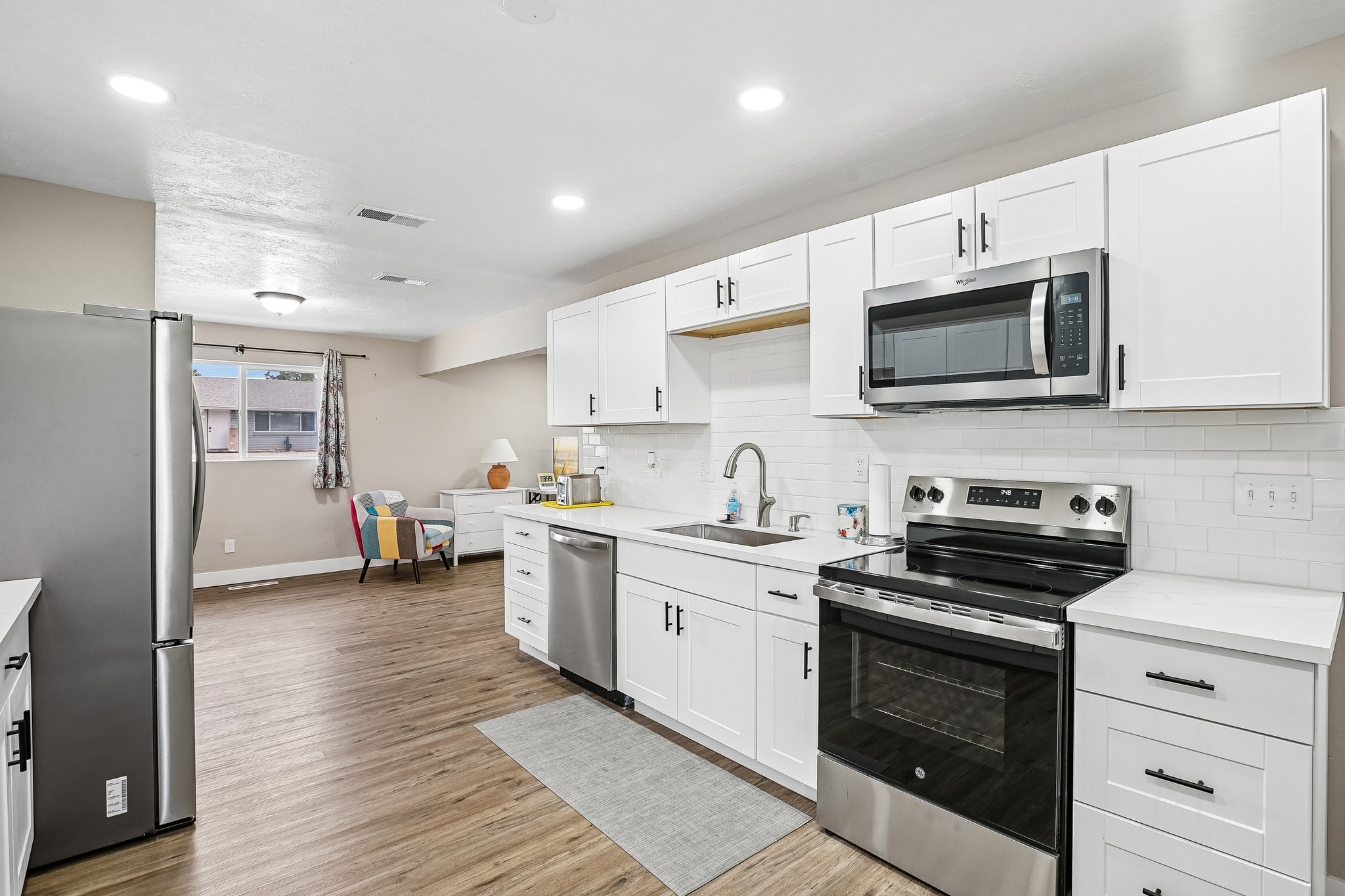 Modern kitchen featuring white shaker cabinetry, stainless steel appliances, white subway tile backsplash, light-toned countertops, and wood-finish flooring