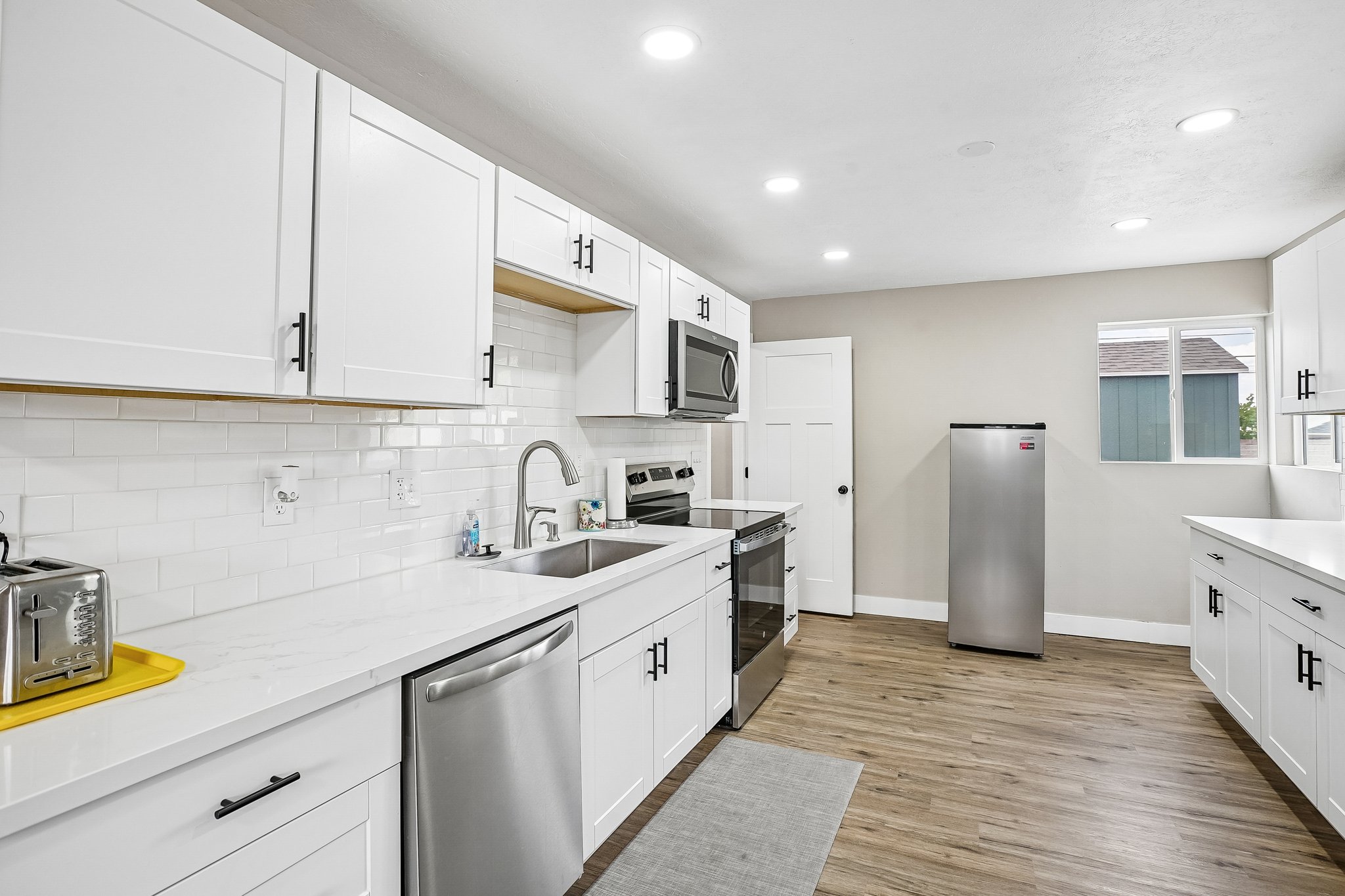 Kitchen featuring white shaker cabinetry, stainless steel appliances, white subway tile backsplash, recessed lighting, and wood-finish flooring