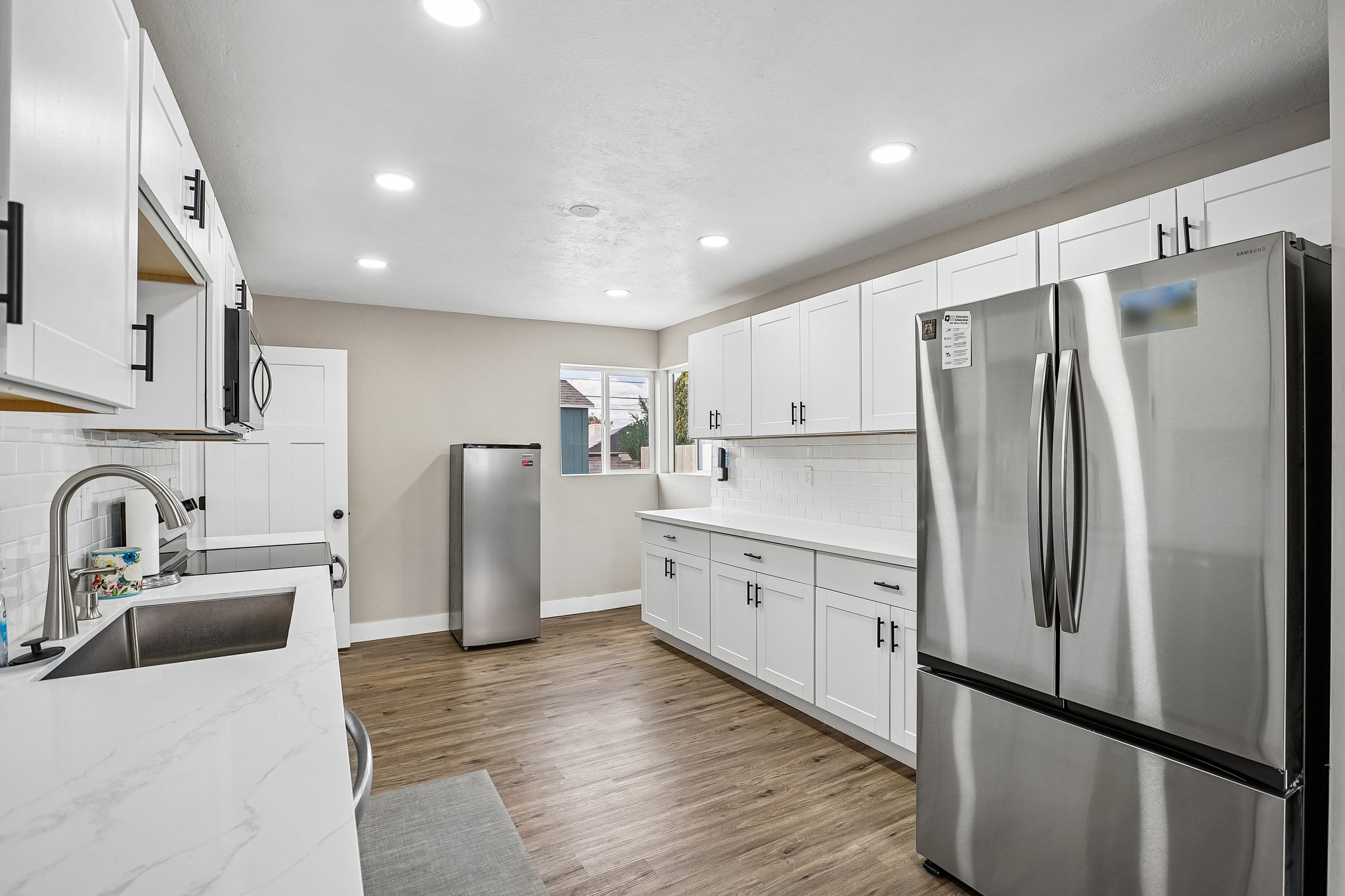 Contemporary kitchen featuring white cabinetry with matte black hardware, white countertops, and wood-finish flooring