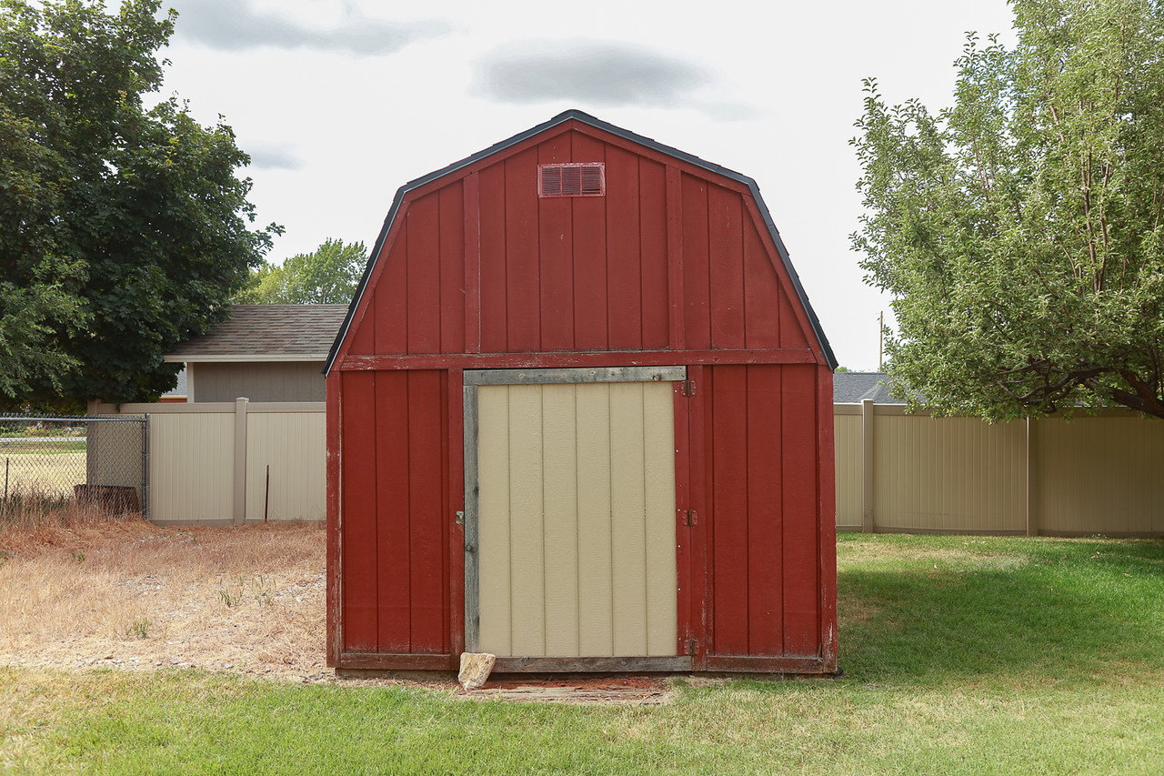 Red wood-sided shed with a gambrel roof and light-colored sliding door