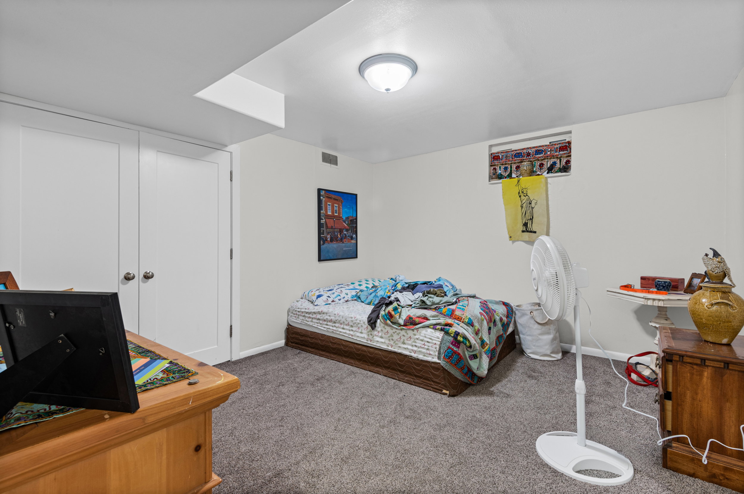 Carpeted room featuring white walls, a flush-mount ceiling light fixture, and a built-in closet with white bifold doors