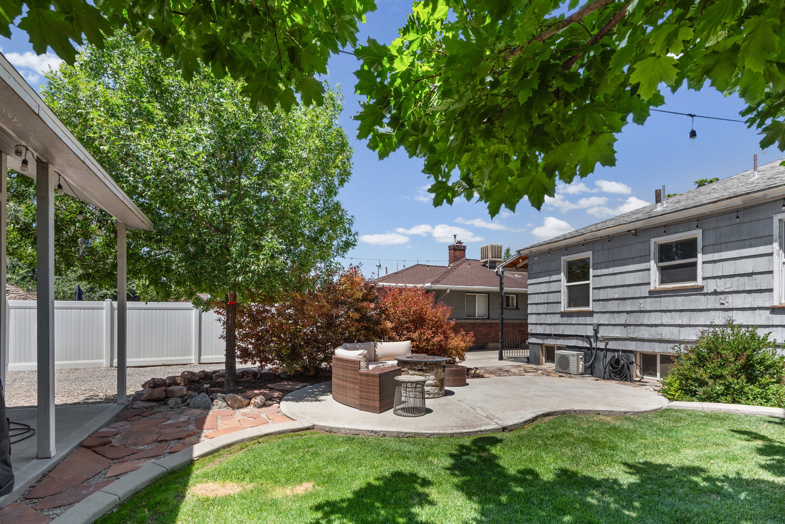 Backyard featuring a shaped concrete patio, a stone path, mature trees, and a manicured lawn
