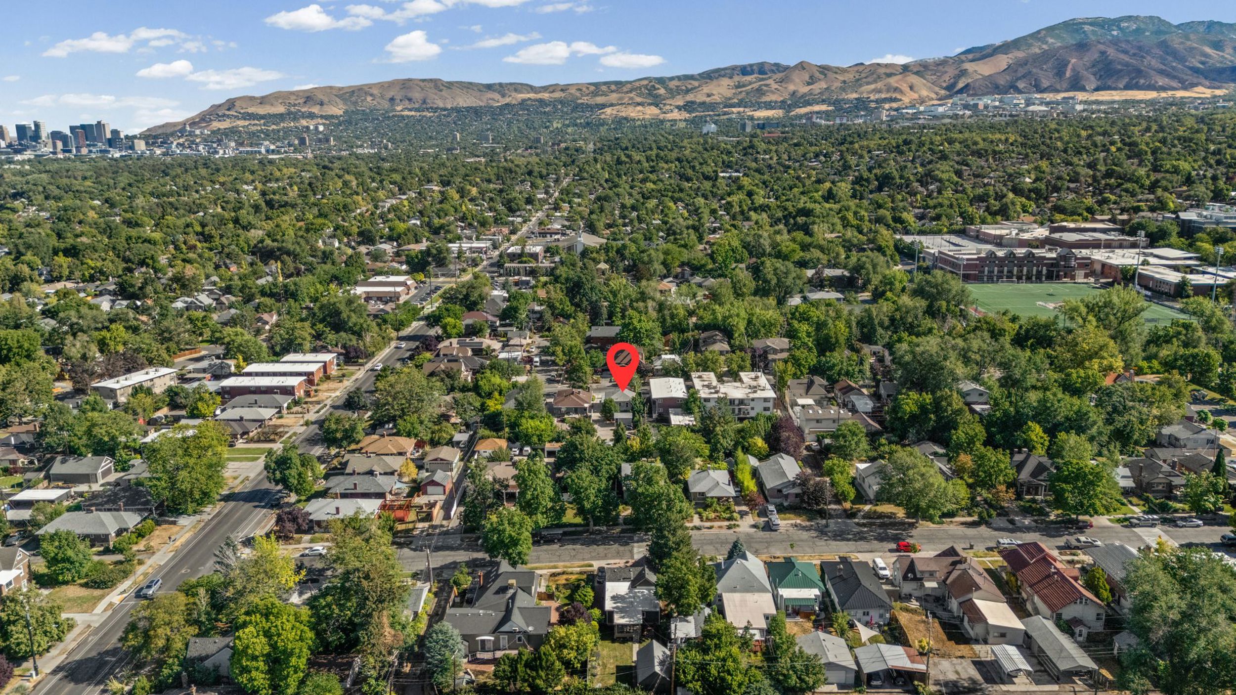 Expansive aerial panorama showcasing a residential neighborhood with abundant mature trees and mountainous terrain in the distance