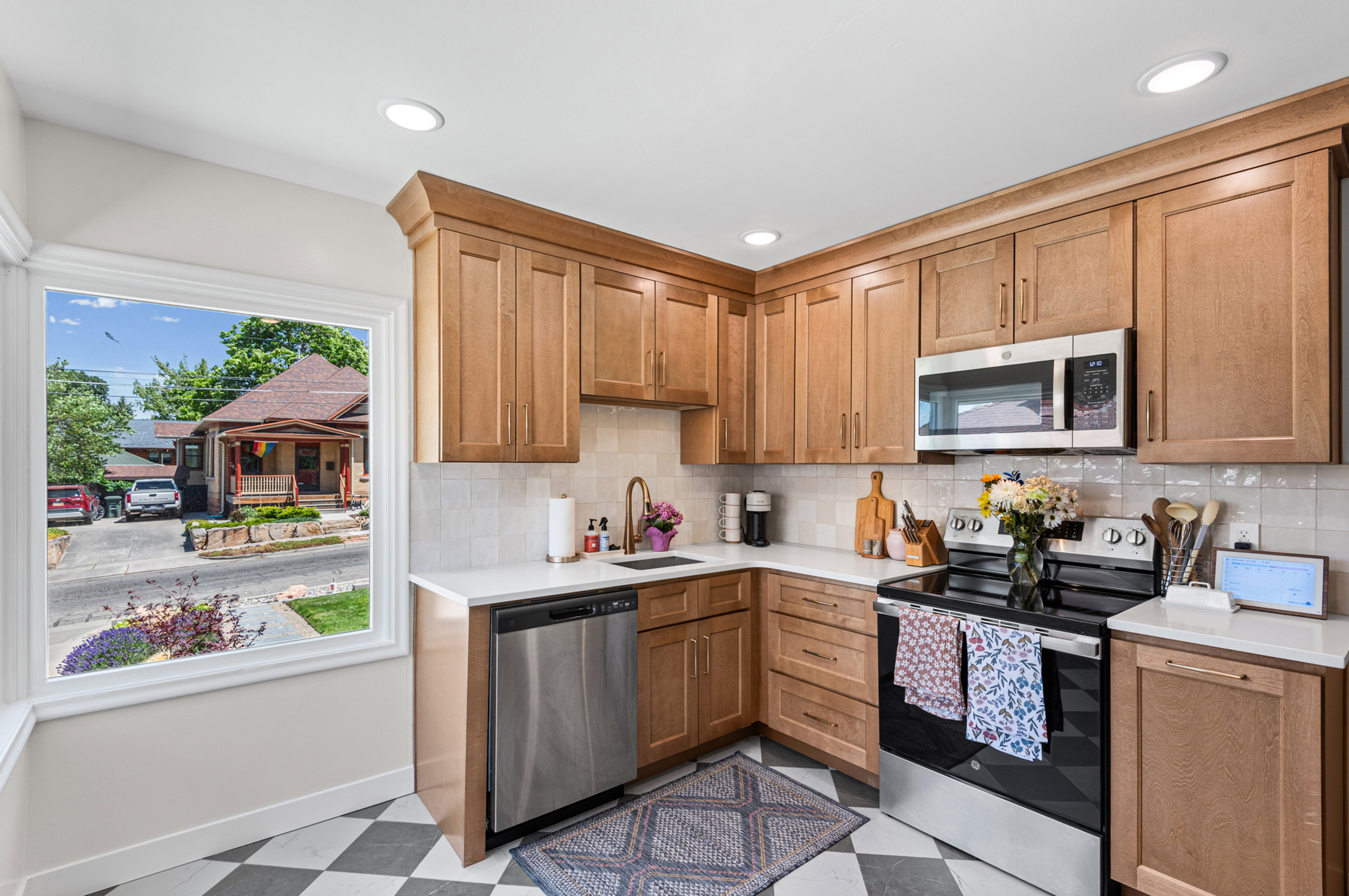 Kitchen featuring wood cabinetry, stainless steel appliances, white countertops, tile backsplash, and checkerboard floor tiling