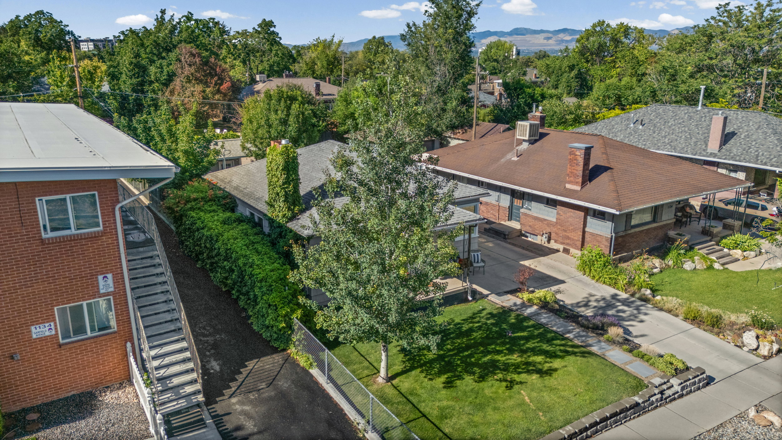 Brick-clad home with a brown shingle roof, integrated carport, and an expansive paved driveway