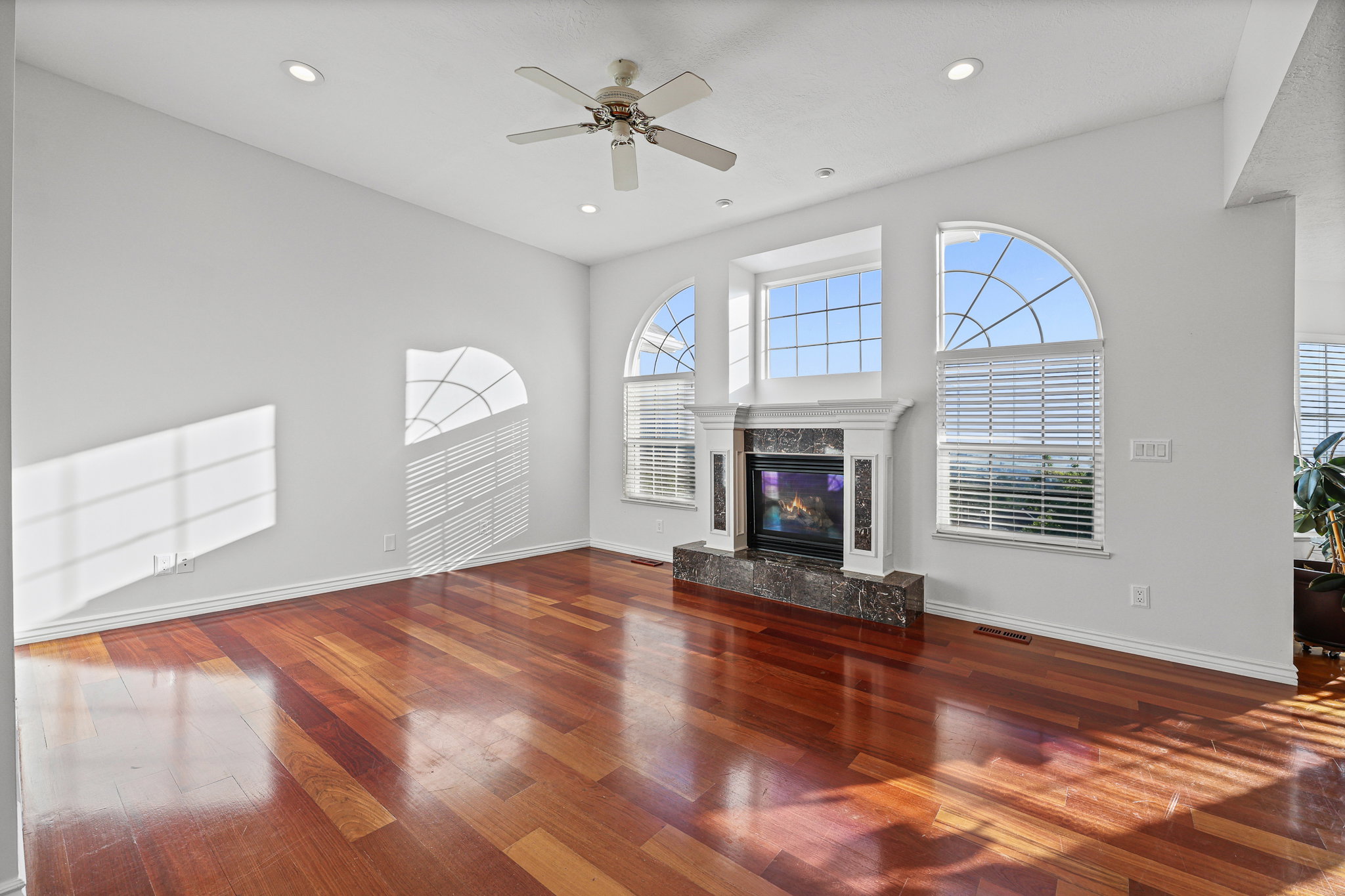 Spacious living area featuring rich wood-finish flooring, a contemporary fireplace with a stone surround, and multiple arched windows