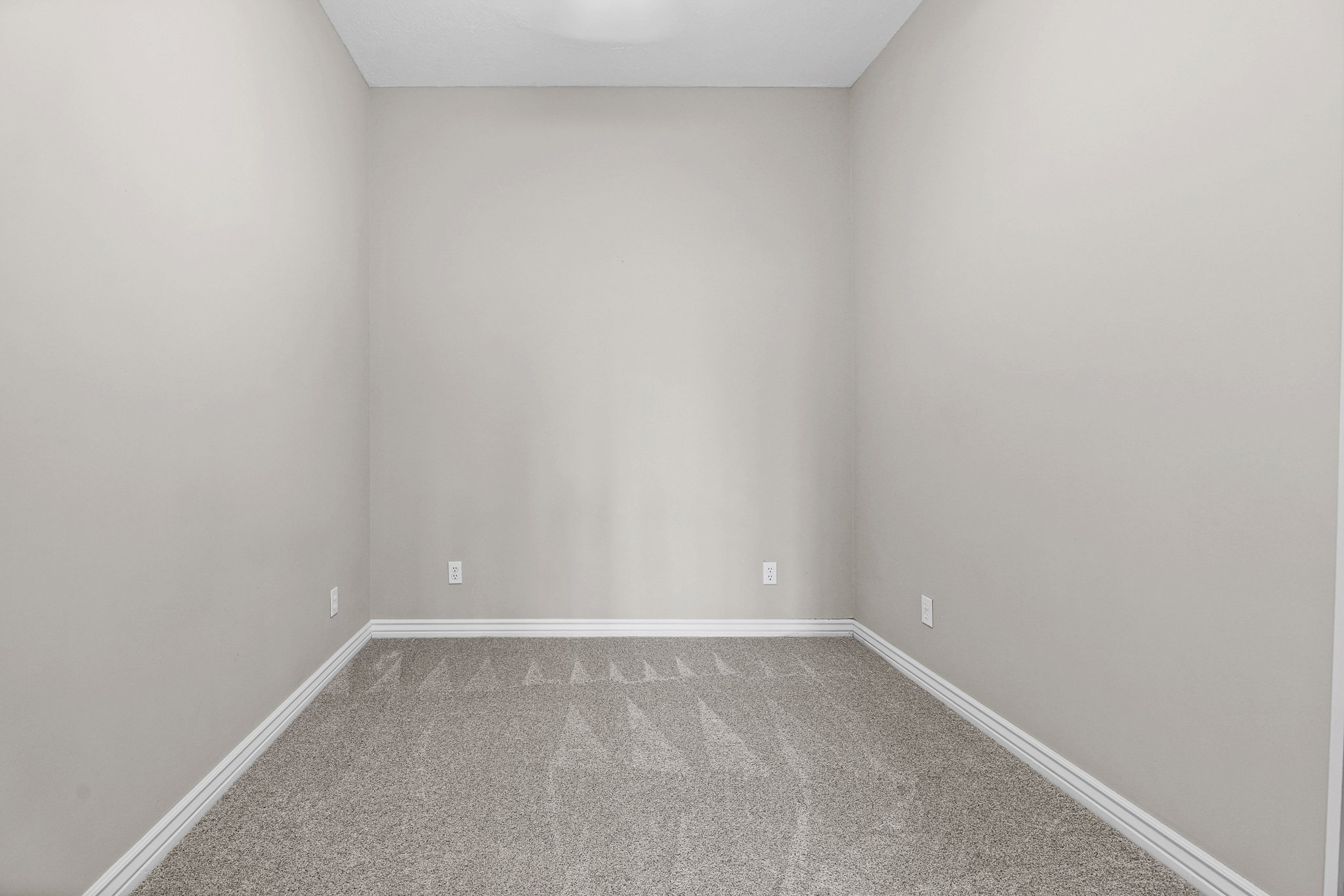 Room featuring neutral-toned walls, gray patterned carpeting, white baseboards, and a ceiling light fixture