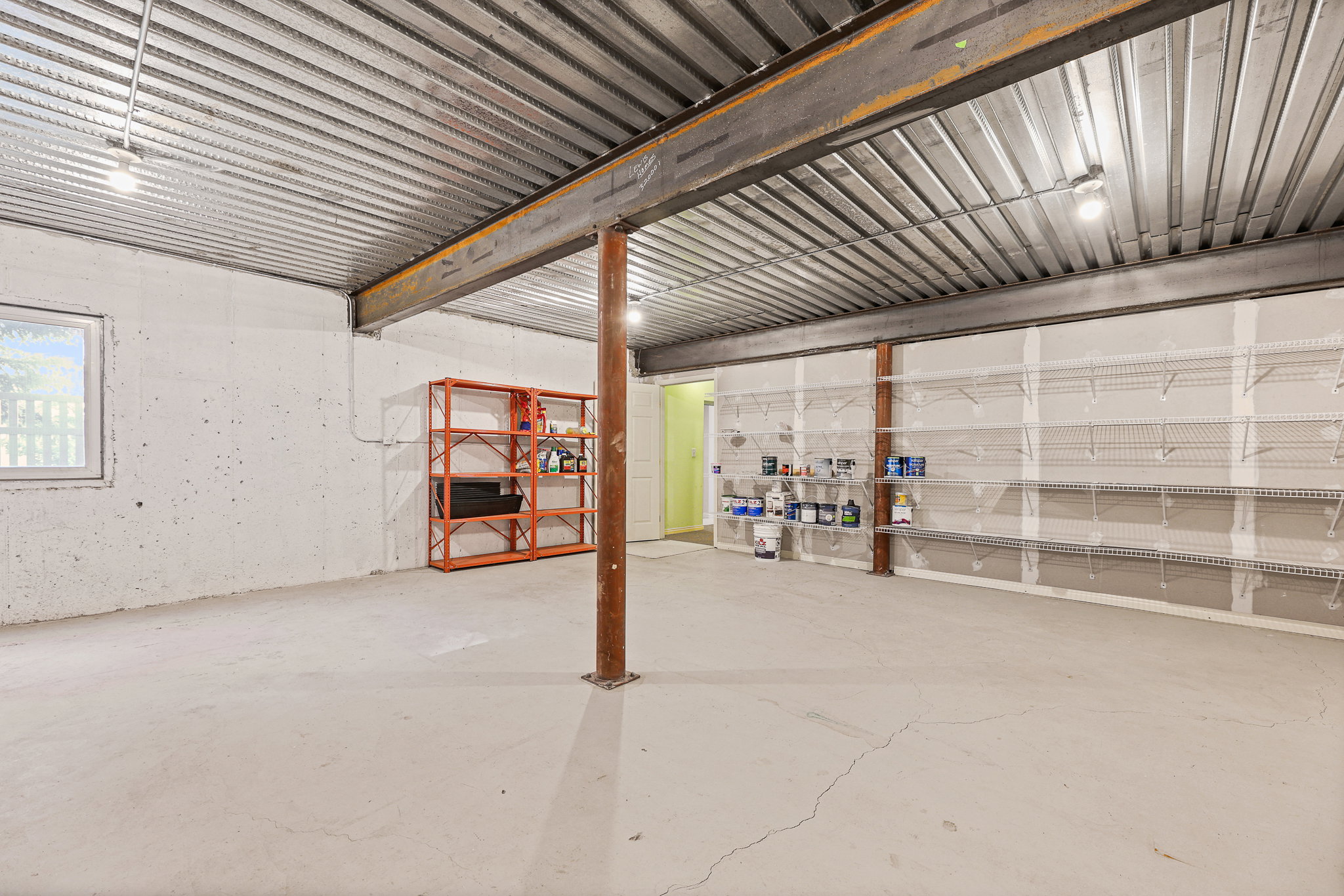 Spacious basement area featuring a concrete floor, exposed metal ceiling, structural support beams, and built-in wall shelving