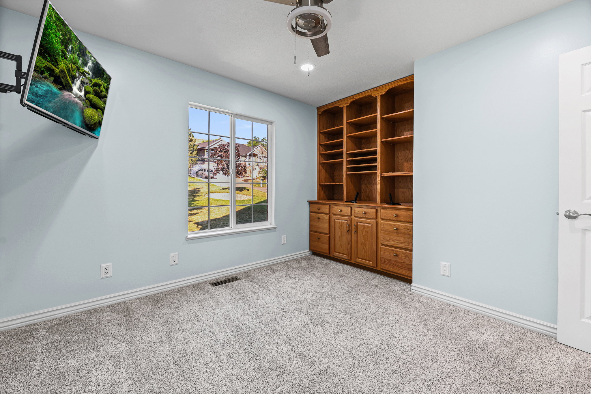 Built-in wood cabinetry with shelving and drawers, light blue walls, and grey carpeted flooring