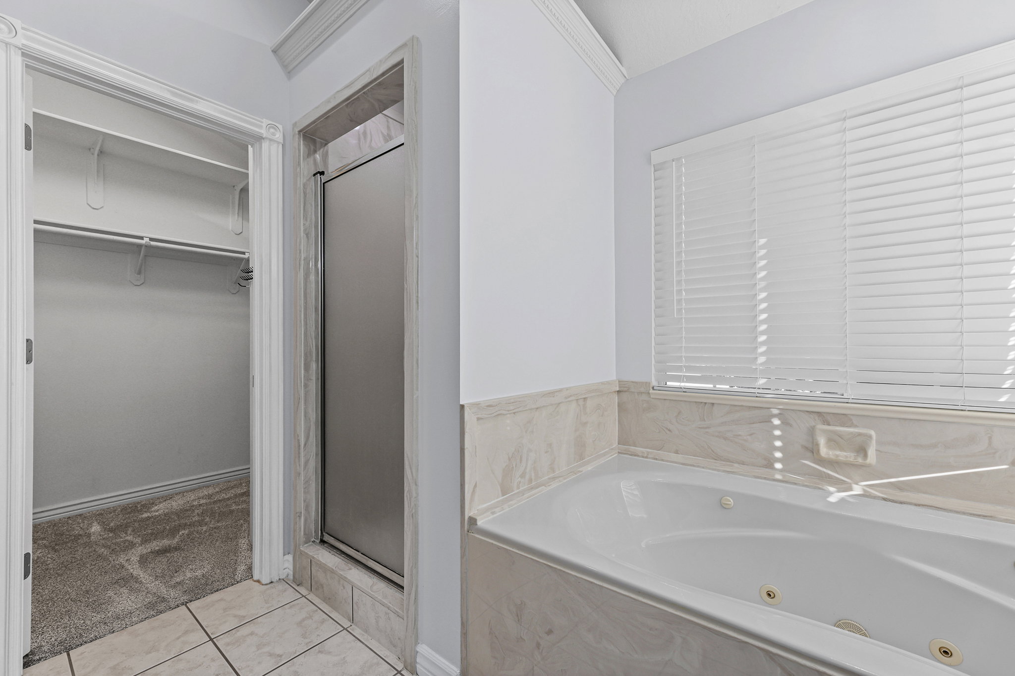 Bathroom featuring a built-in jetted tub, tiled surround, glass-enclosed shower, and a walk-in closet with carpeted flooring