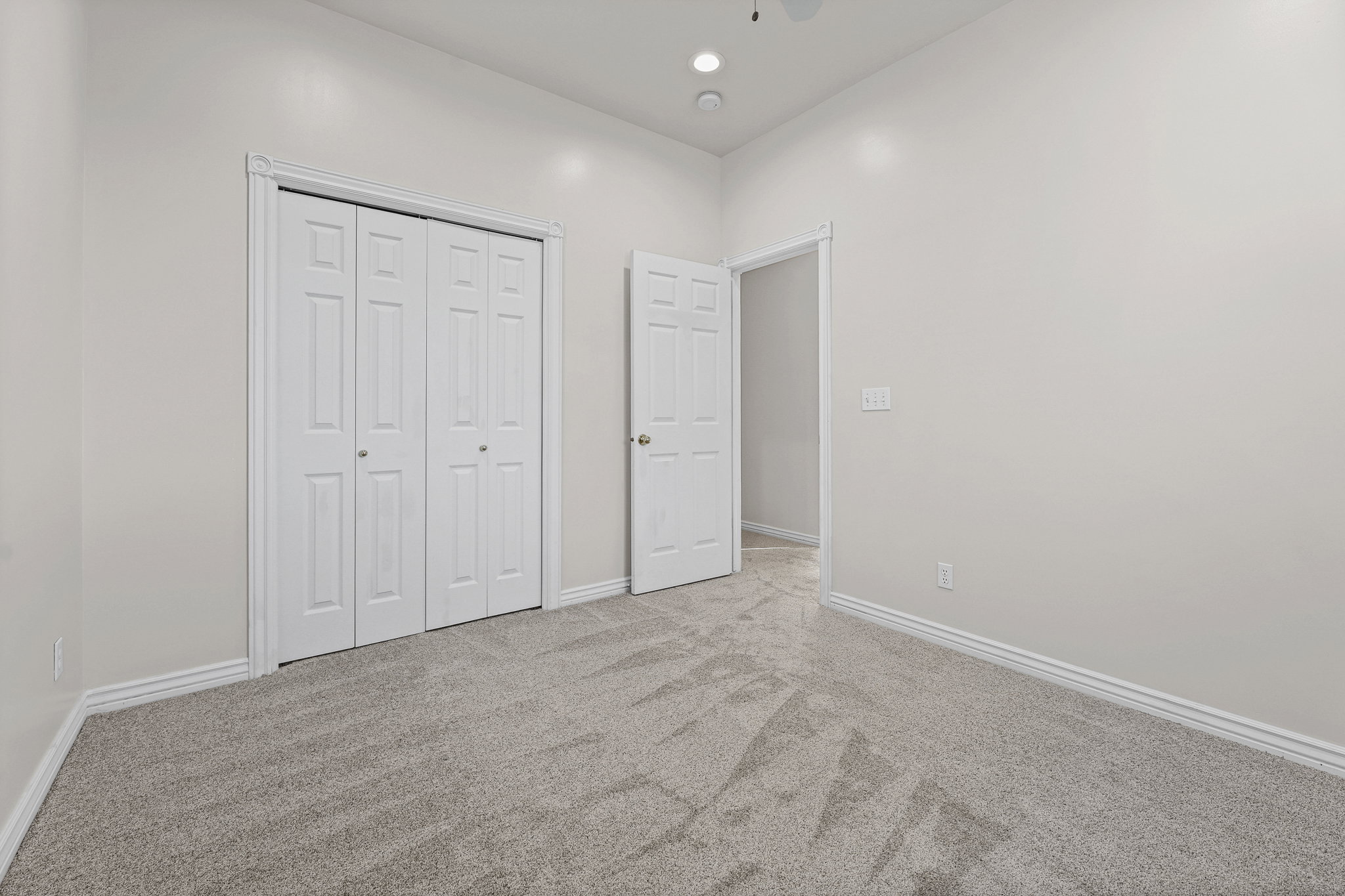 Neutral-toned room featuring a patterned grey carpet, white baseboards, and a white bi-fold closet door
