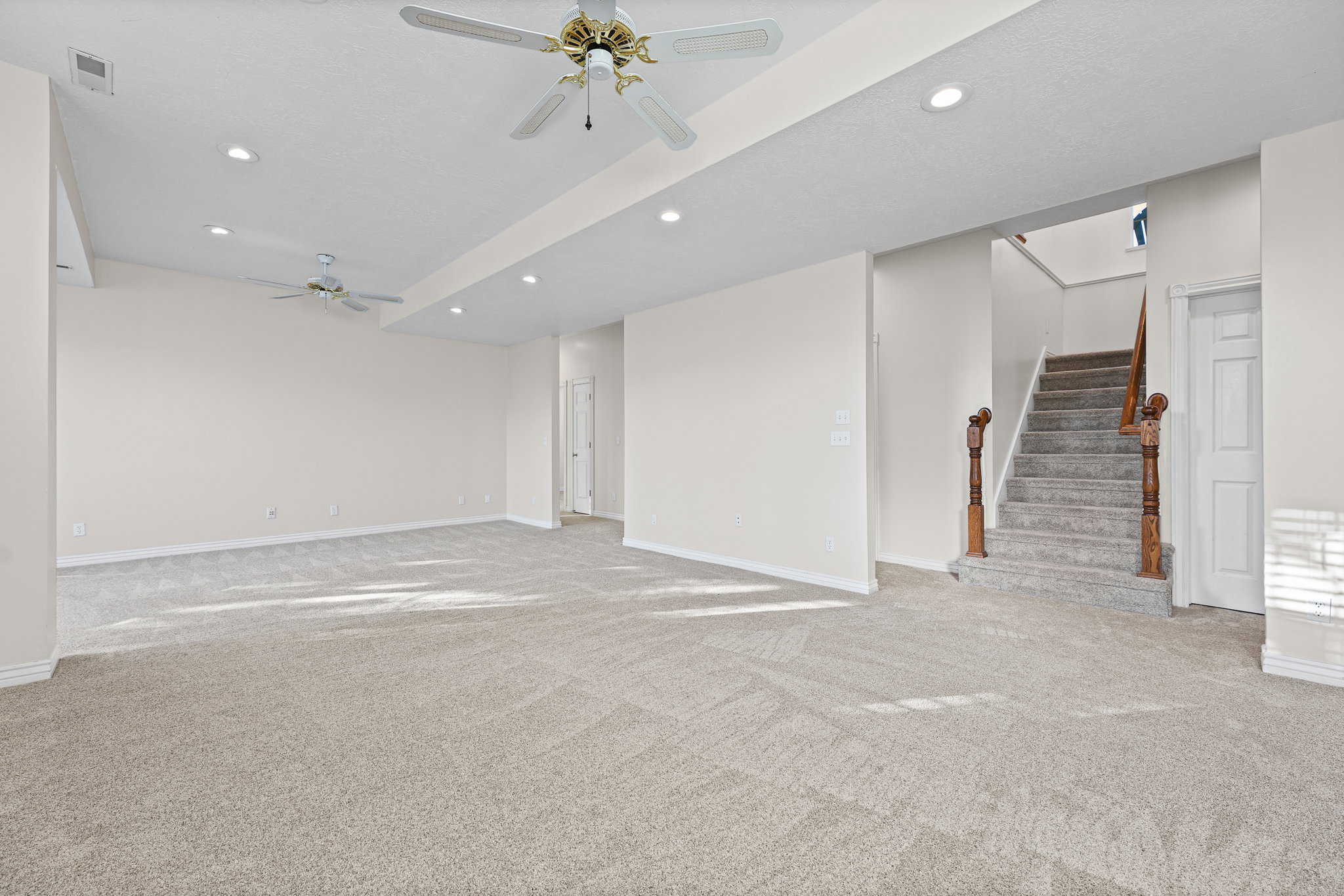Spacious carpeted room featuring recessed lighting and two ceiling fans