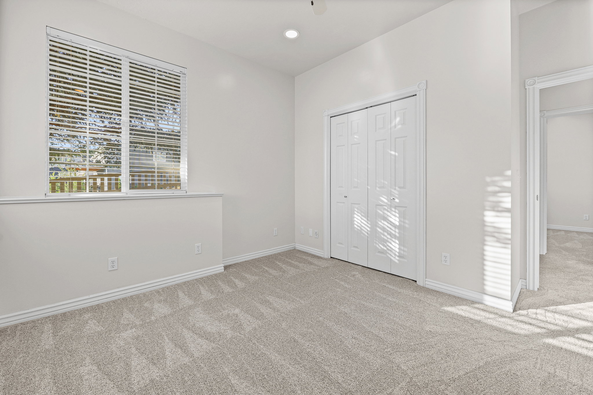 Carpeted room featuring a window with horizontal blinds, bi-fold closet doors, recessed ceiling lighting, and crisp white trim