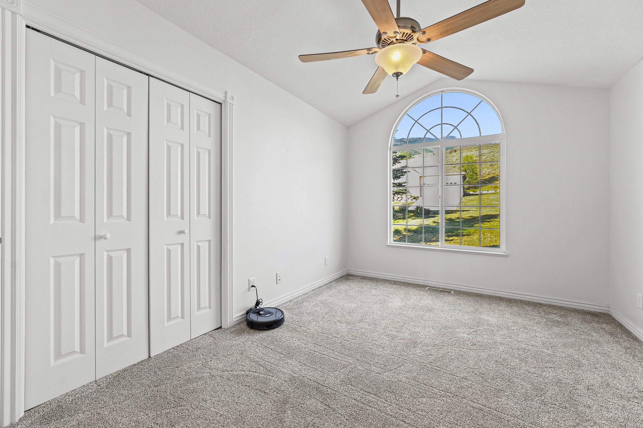 Arched window with grilles providing natural light, accompanied by neutral carpeting and white walls