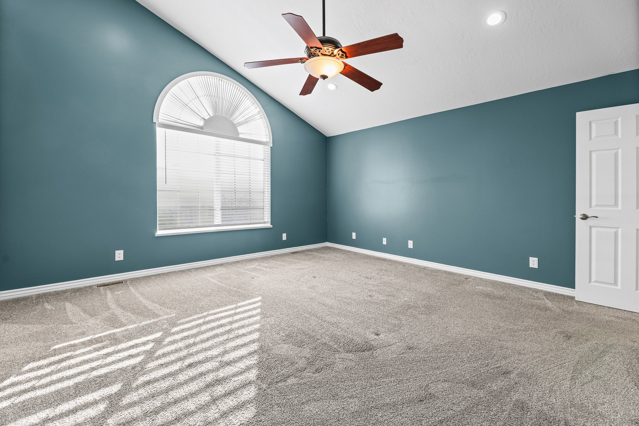 Carpeted room featuring an arched window, vaulted ceiling, ceiling fan, recessed lighting, and a paneled door