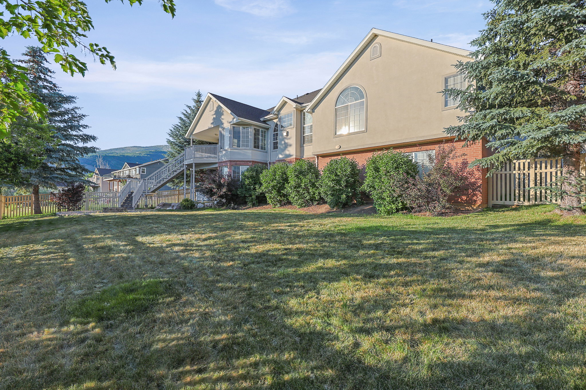 Expansive rear lawn featuring mature evergreen trees and a wood picket fence