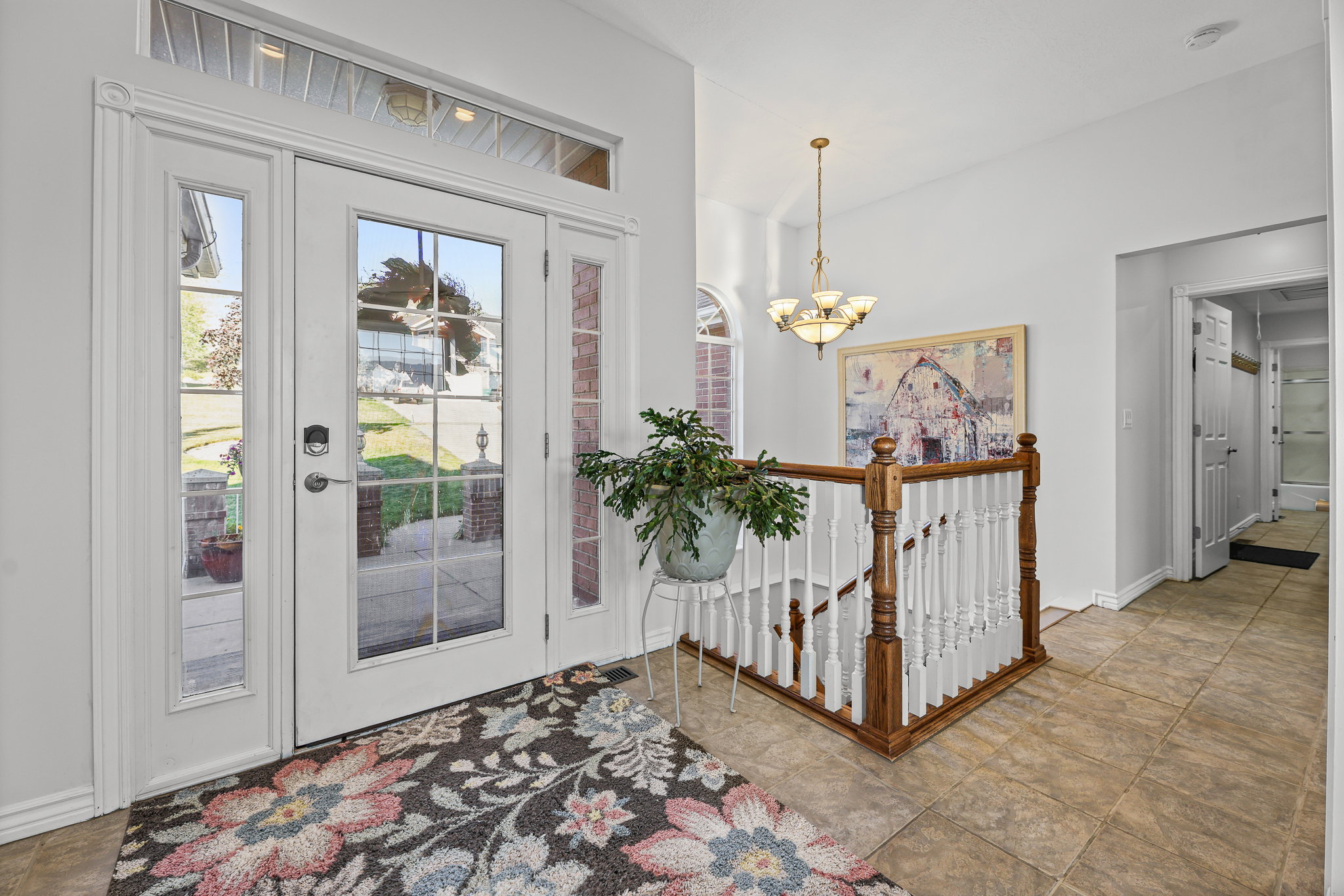 Entryway featuring double glass-panel doors with sidelights and a transom window, a tiled floor, and a staircase with a wood handrail and white balusters