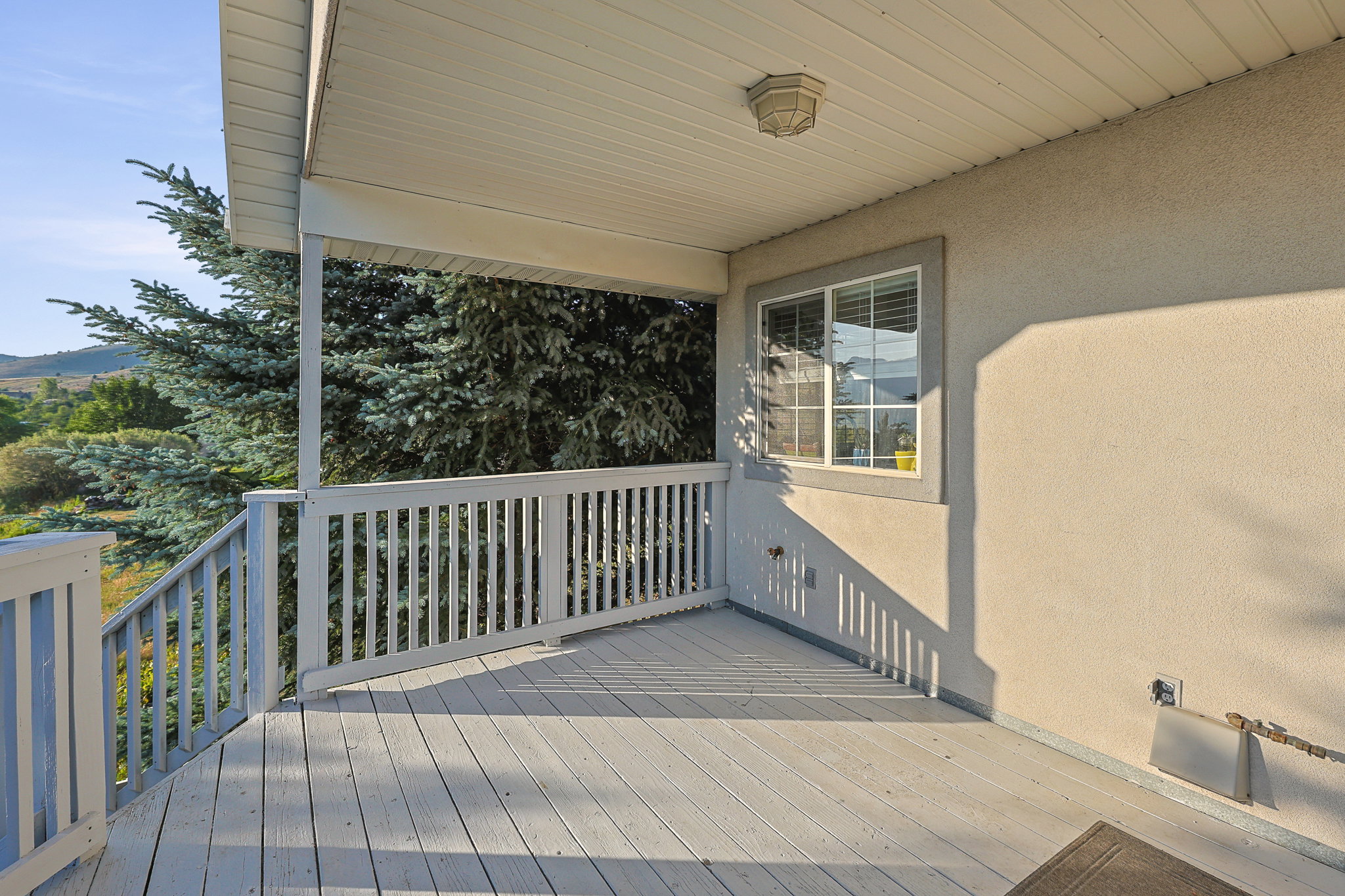 Covered deck featuring a light-toned stucco exterior, white window trim, and painted railing