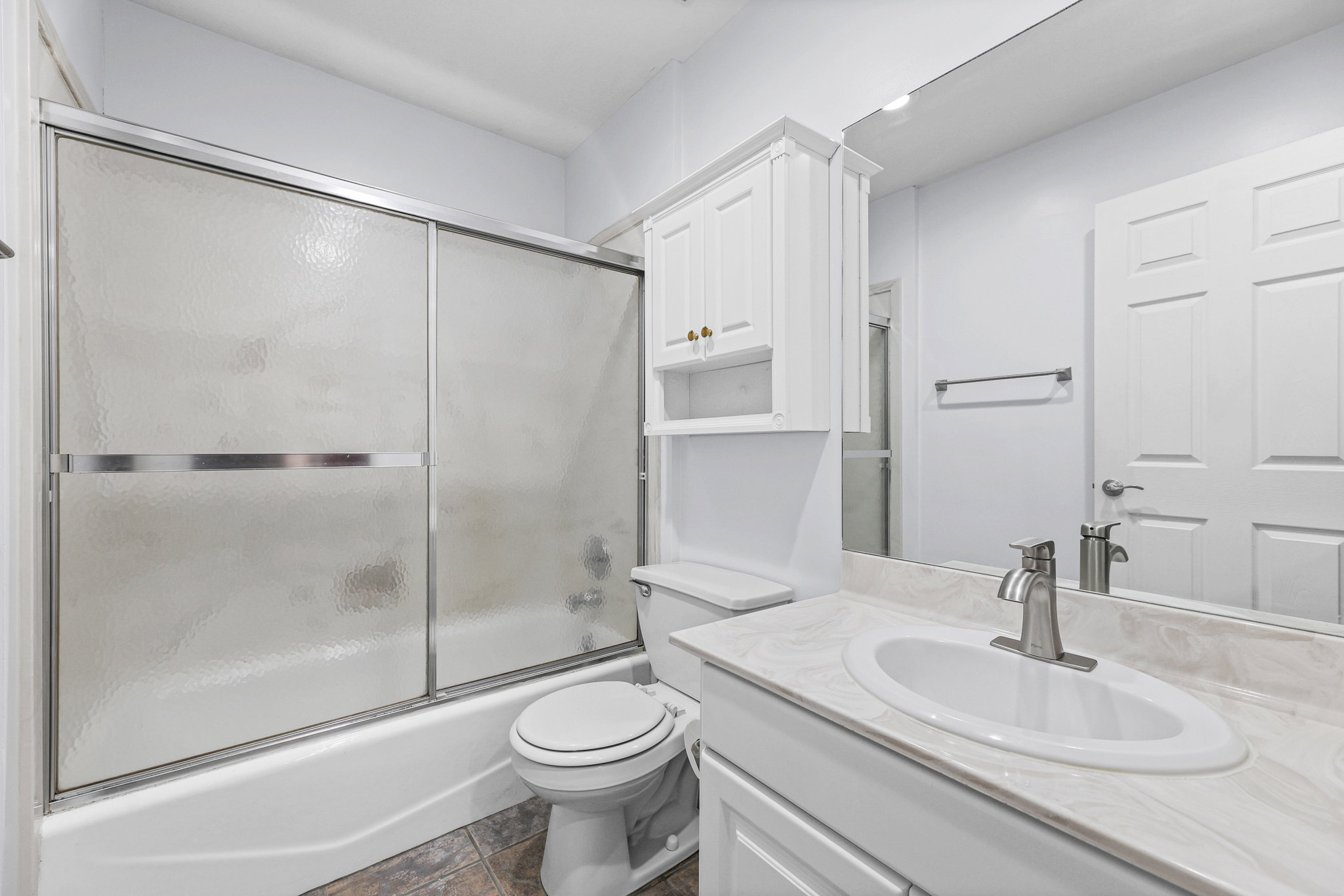 Bathroom featuring a full-size tub with sliding frosted glass doors, a vanity with an integrated sink and light-toned countertop, a wall-mounted medicine cabinet with gold-toned hardware, and mosaic-style floor tiling