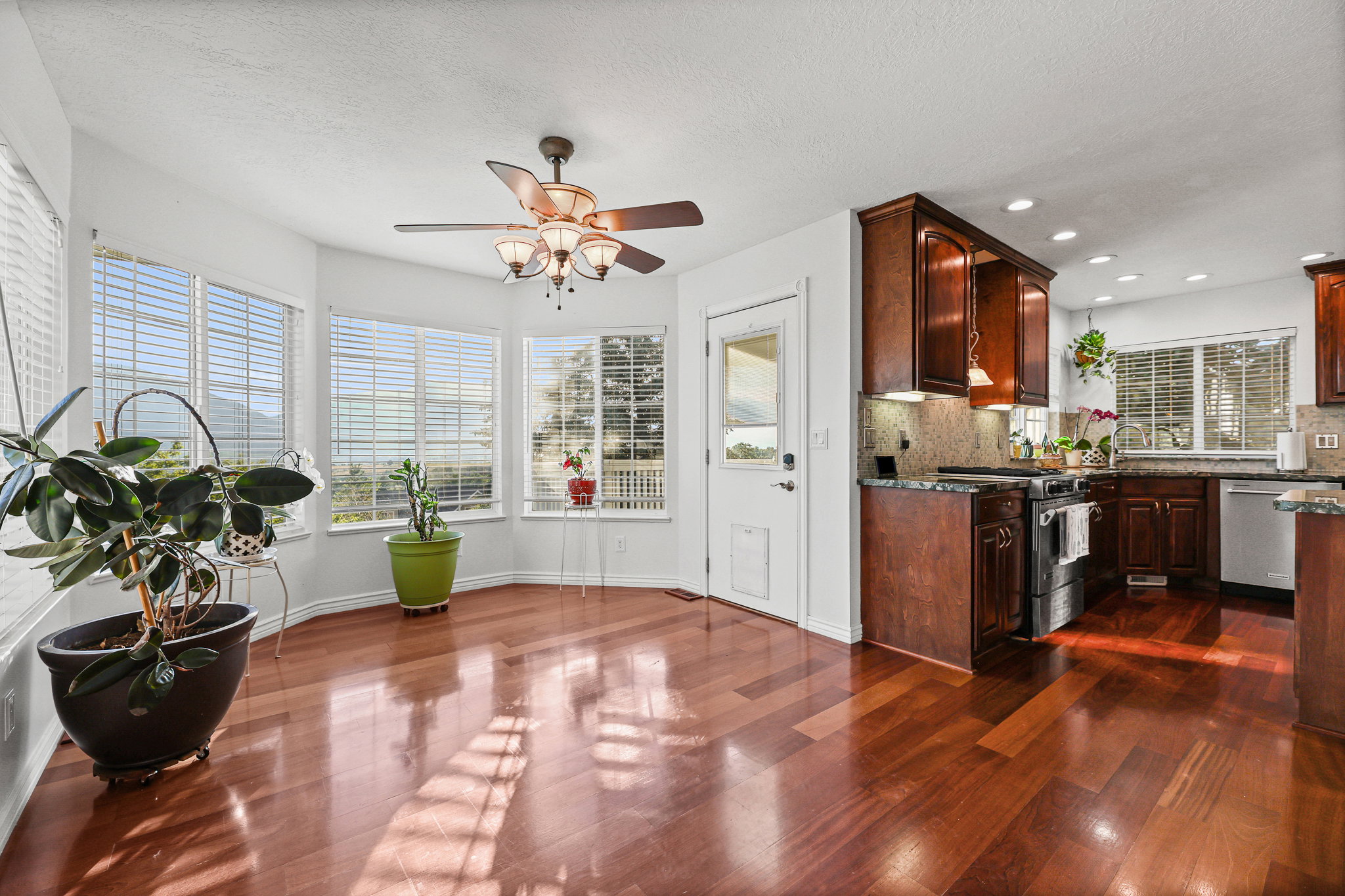 Bay window dining area featuring wood-finish flooring, a ceiling fan with integrated lighting, and direct access to the kitchen