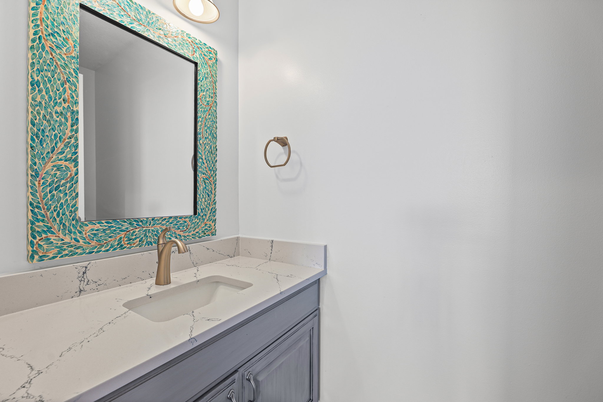 Vanity featuring a patterned mirror, single basin sink, and brass-finish faucet