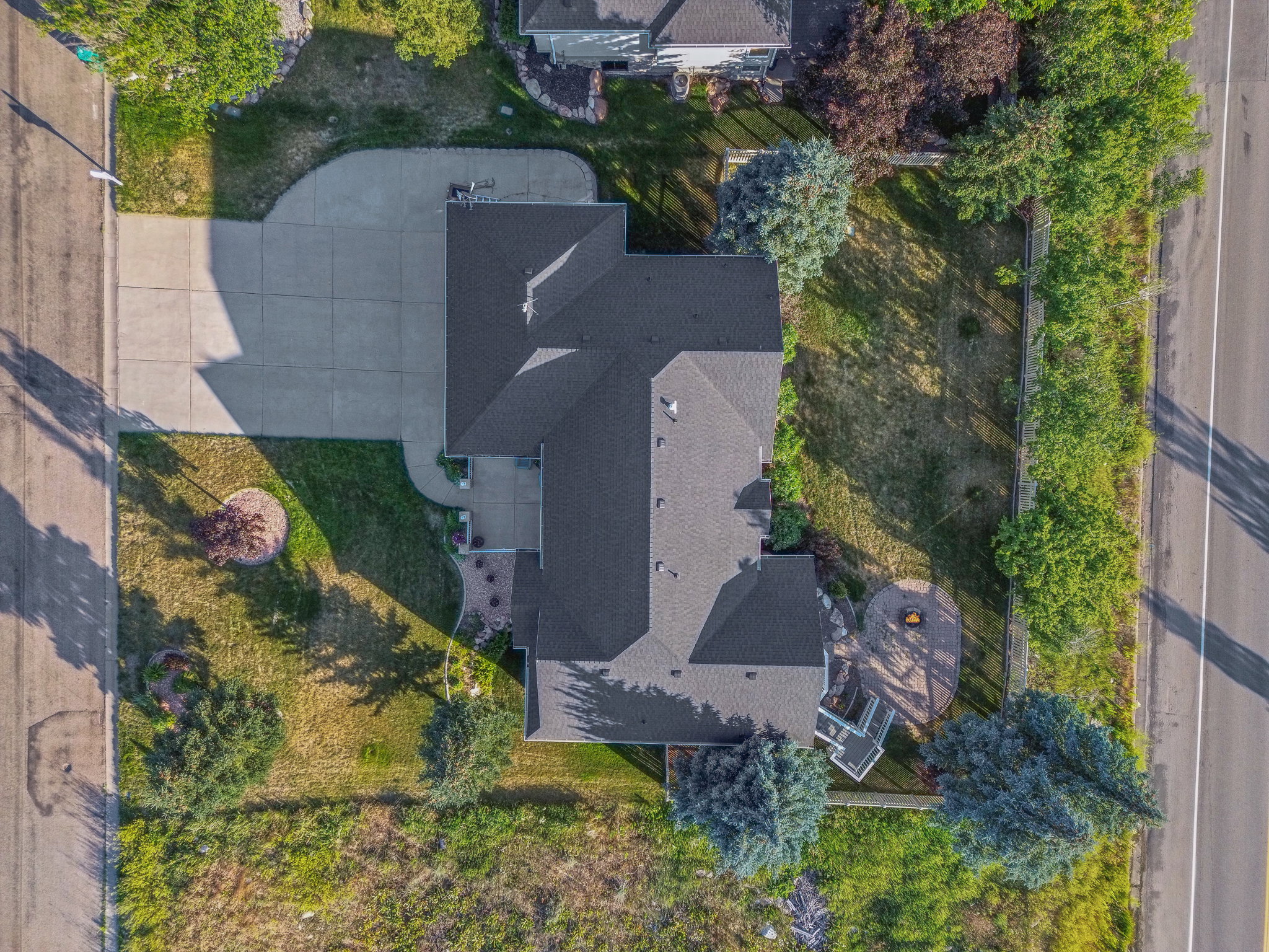 Spacious property featuring a large concrete driveway, mature trees, and a private rear patio with a built-in fire pit