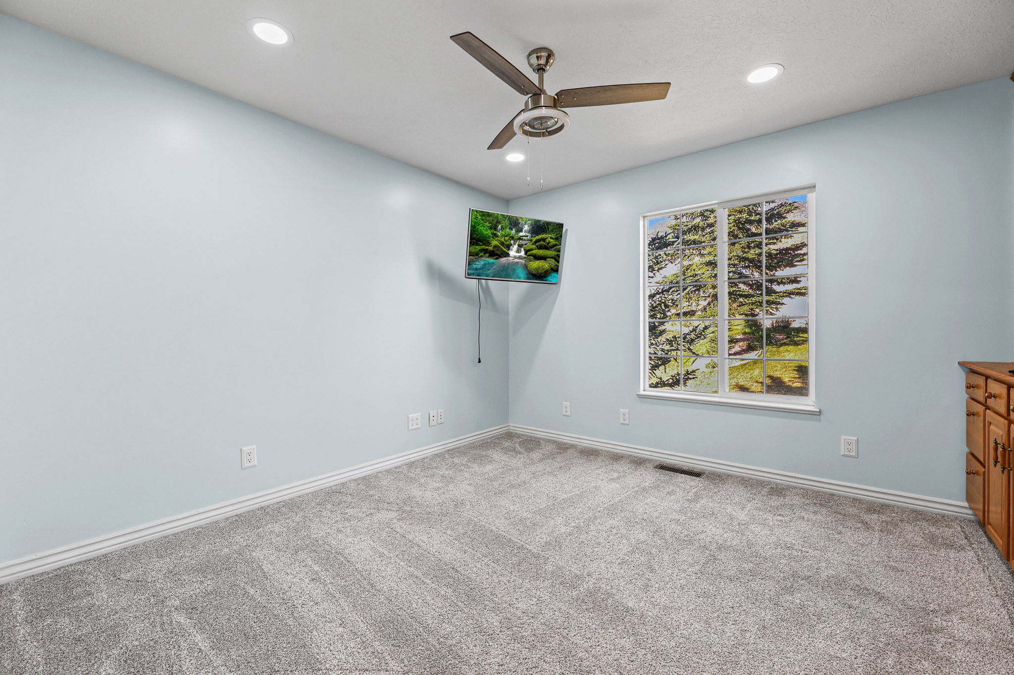 Light blue interior wall paint, recessed ceiling lighting, a ceiling fan, a window, and wood cabinetry