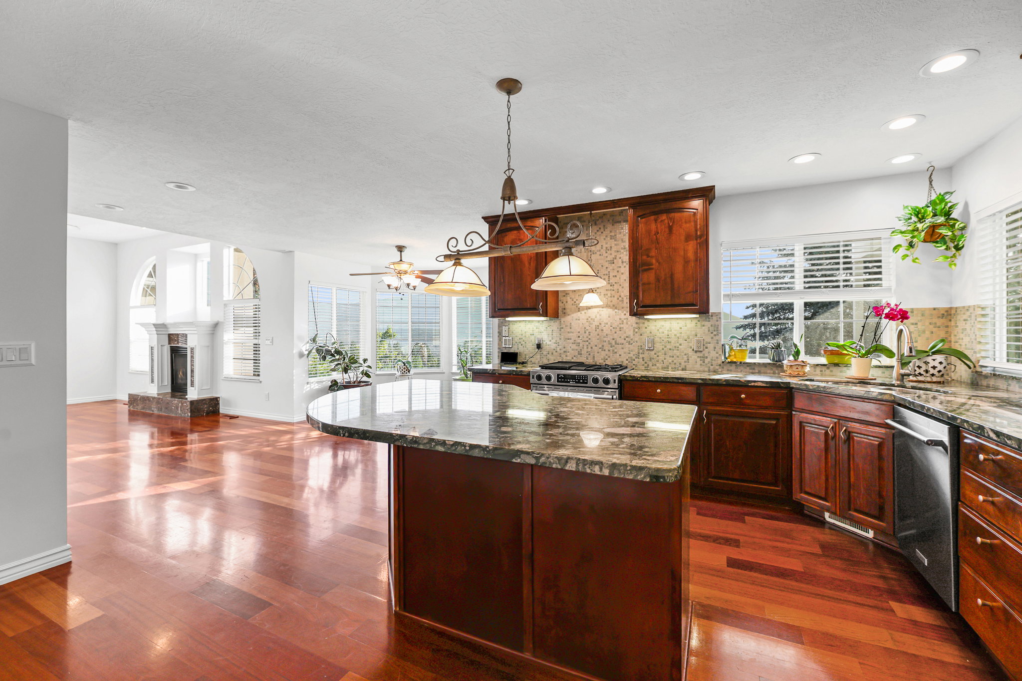 Spacious kitchen featuring an expansive island with a stone countertop, rich wood cabinetry, stainless steel appliances, and wood-finish flooring throughout