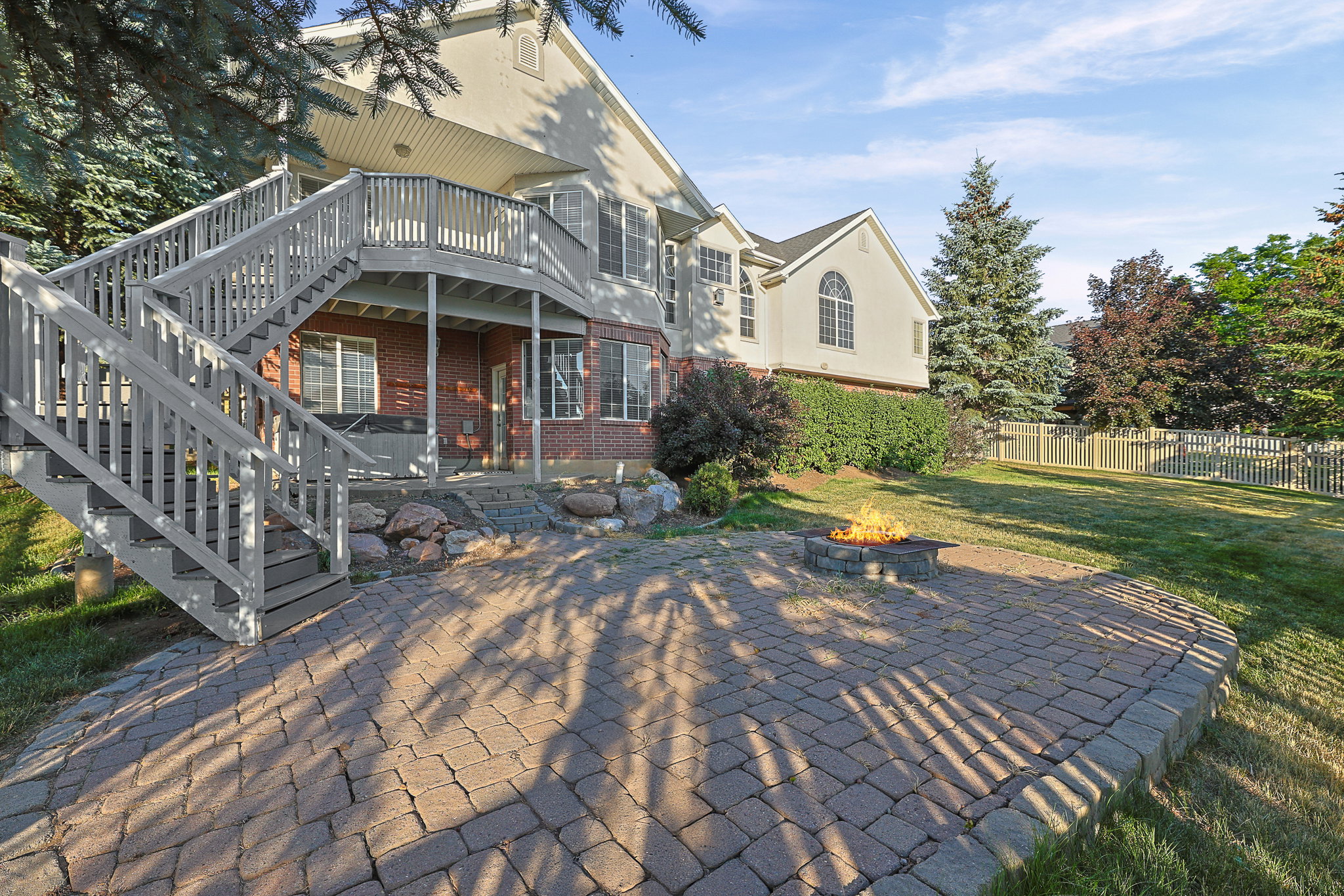 Expansive backyard featuring a paver patio with a built-in fire pit, a tiered wooden deck with stairs, a hot tub, and a manicured lawn
