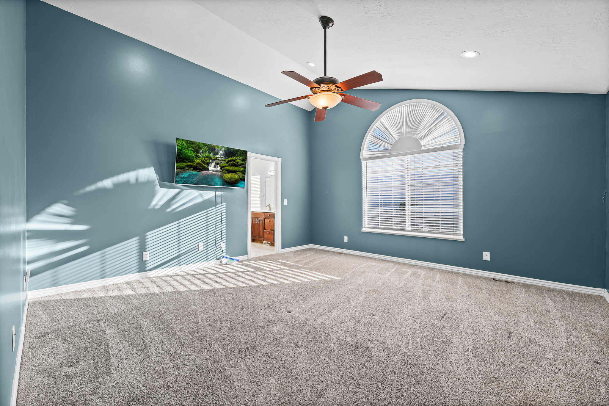 Spacious room featuring vaulted ceilings, a ceiling fan with integrated lighting, recessed lighting, an arched window with blinds, and neutral-toned carpeting