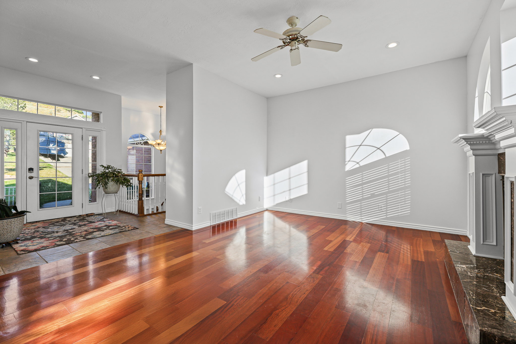 Expansive living area featuring polished wood-finish flooring, a decorative fireplace with a marble-finish hearth, a ceiling fan, and recessed lighting