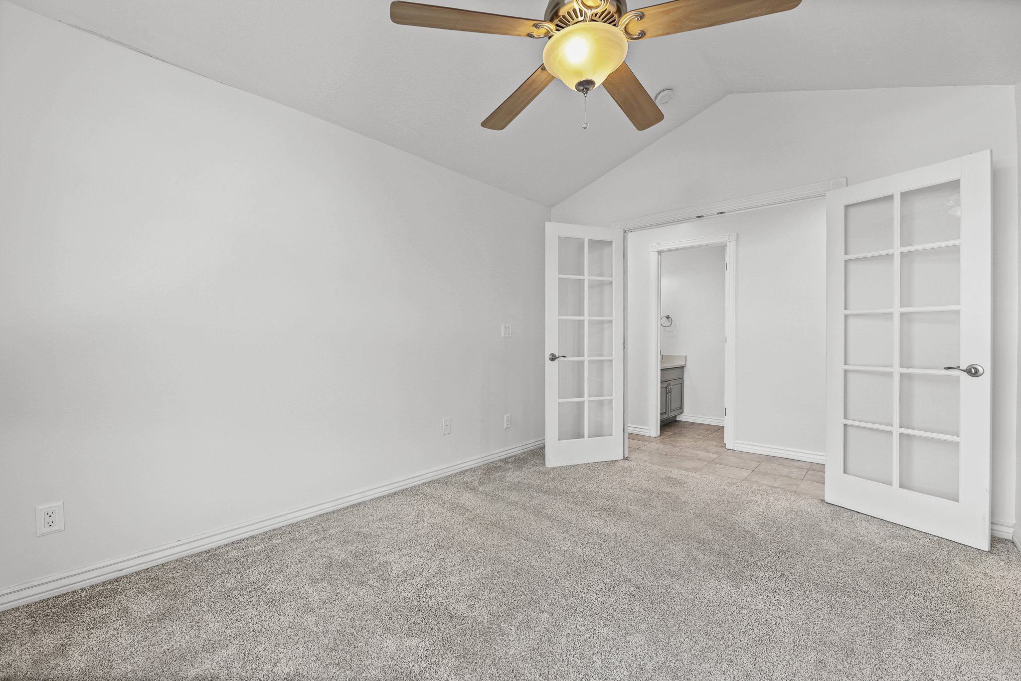 Carpeted room featuring a ceiling fan with integrated lighting, vaulted ceiling, and French doors