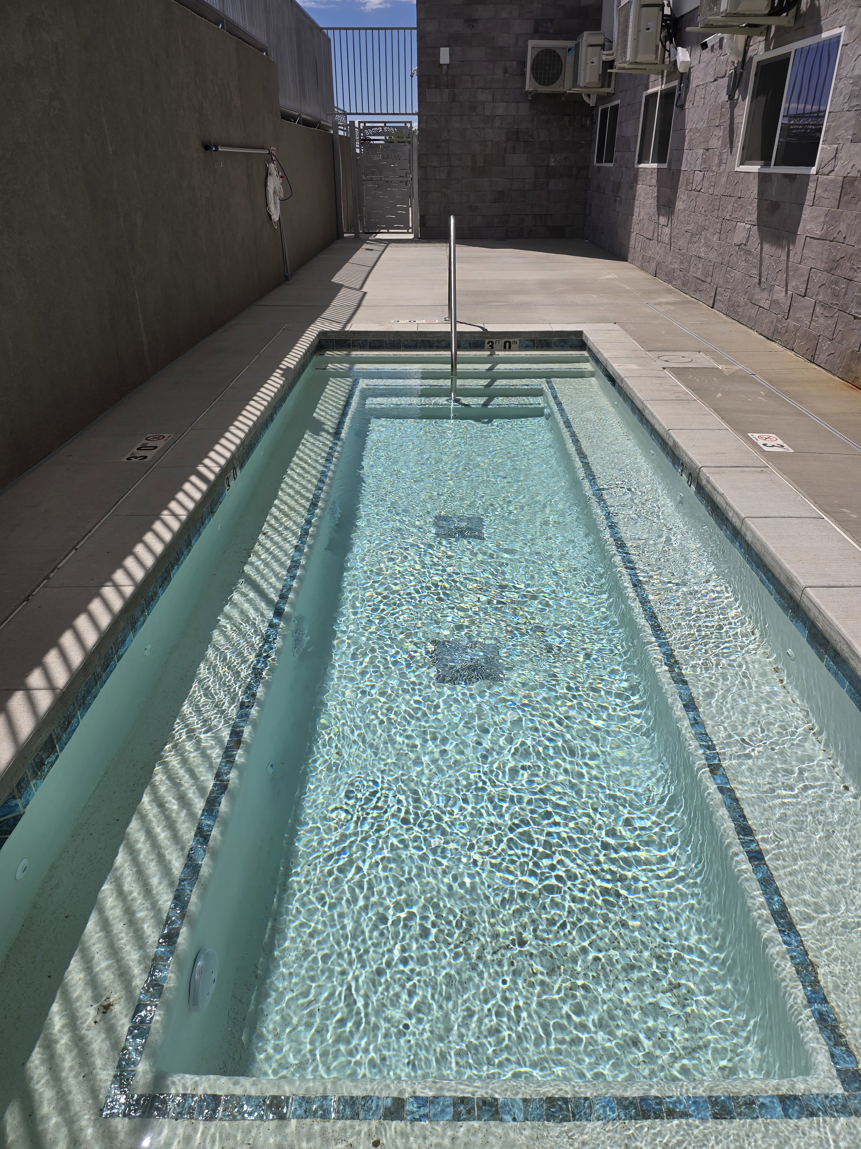 Rectangular wading pool with tiled steps, a stainless steel handrail, and mosaic tile detailing