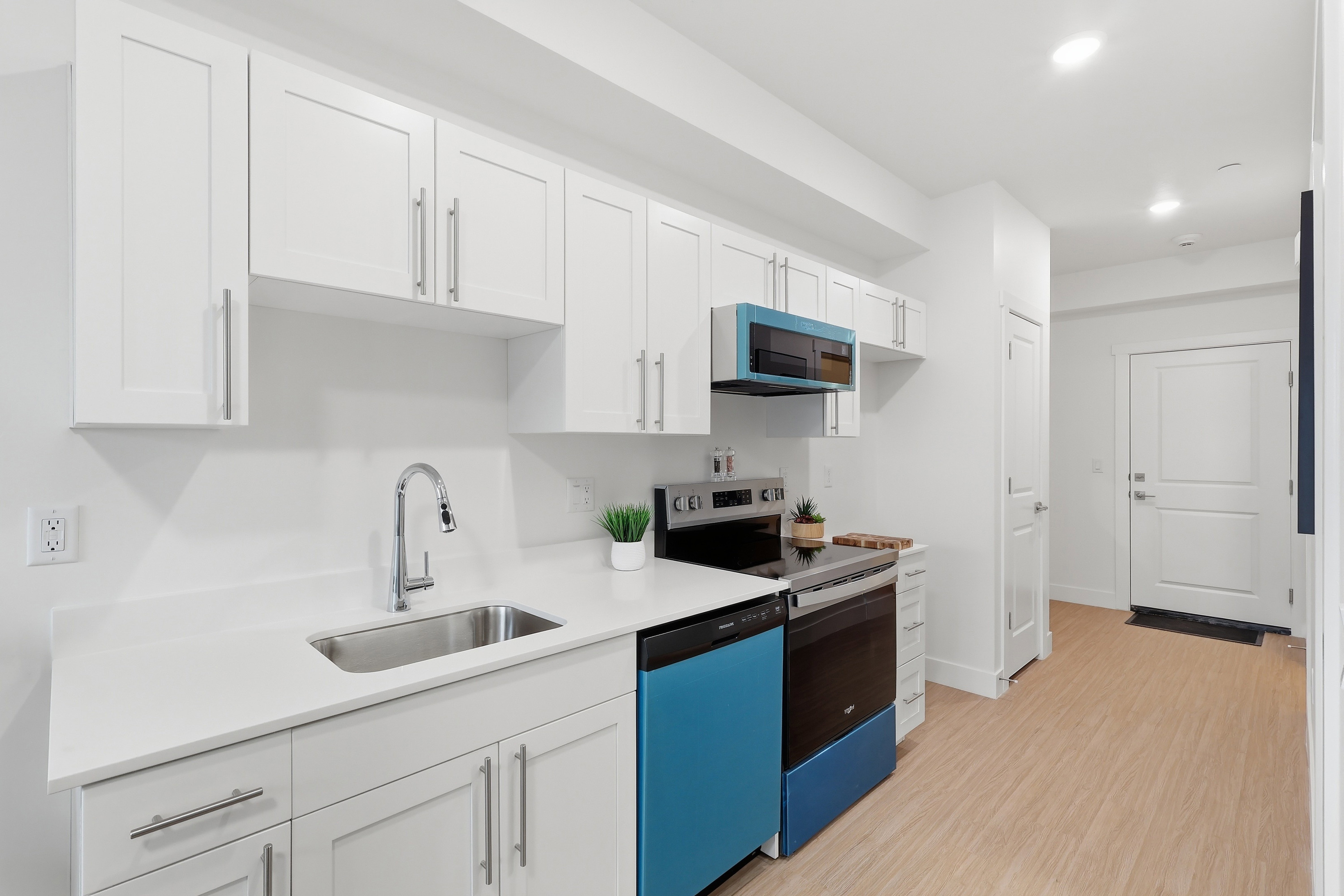 Modern kitchen featuring white shaker cabinetry, stainless steel sink, light-toned countertops, and light wood-finish flooring
