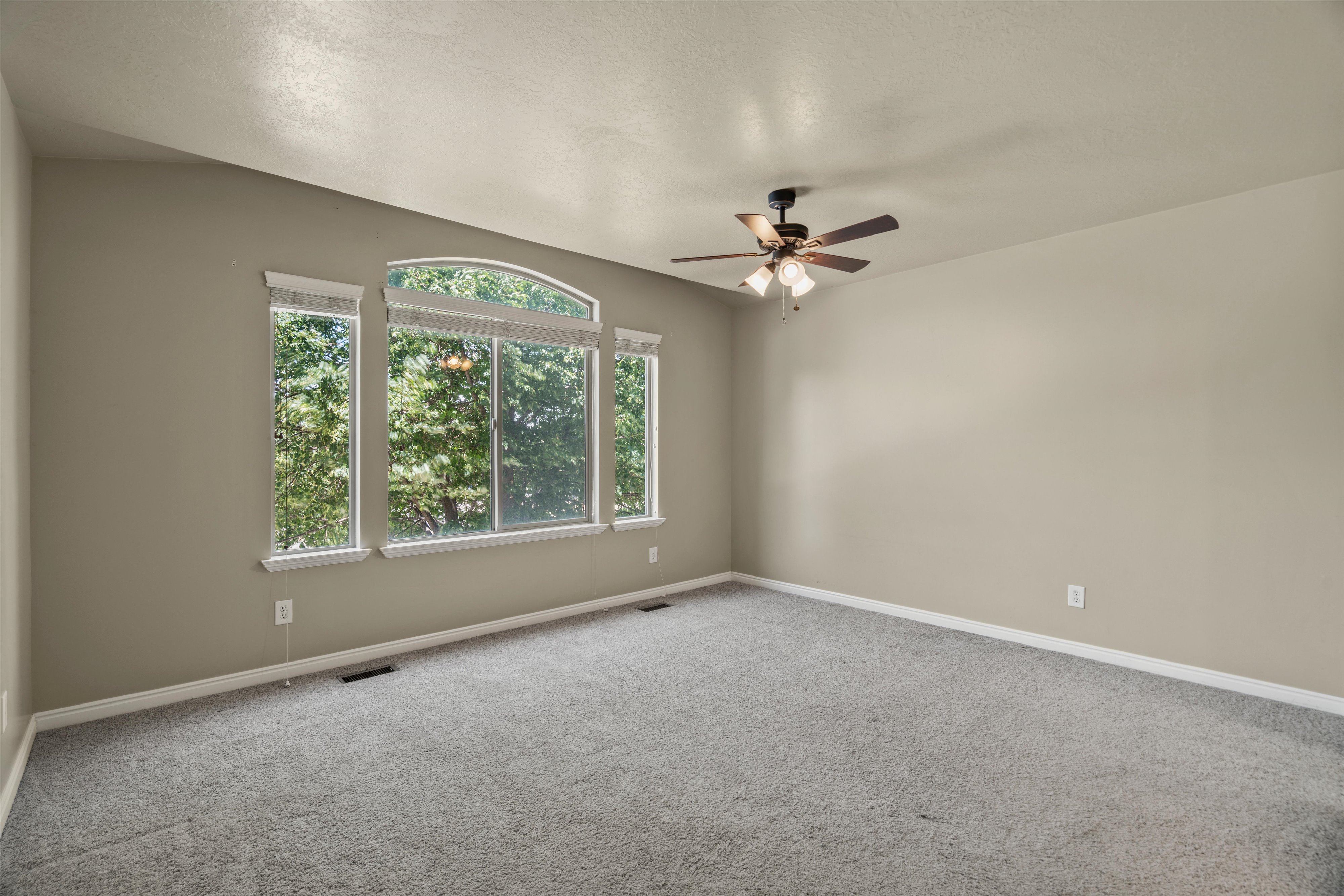 Spacious room featuring a multi-pane window with an arched transom, a ceiling fan with integrated lighting, and neutral wall paint