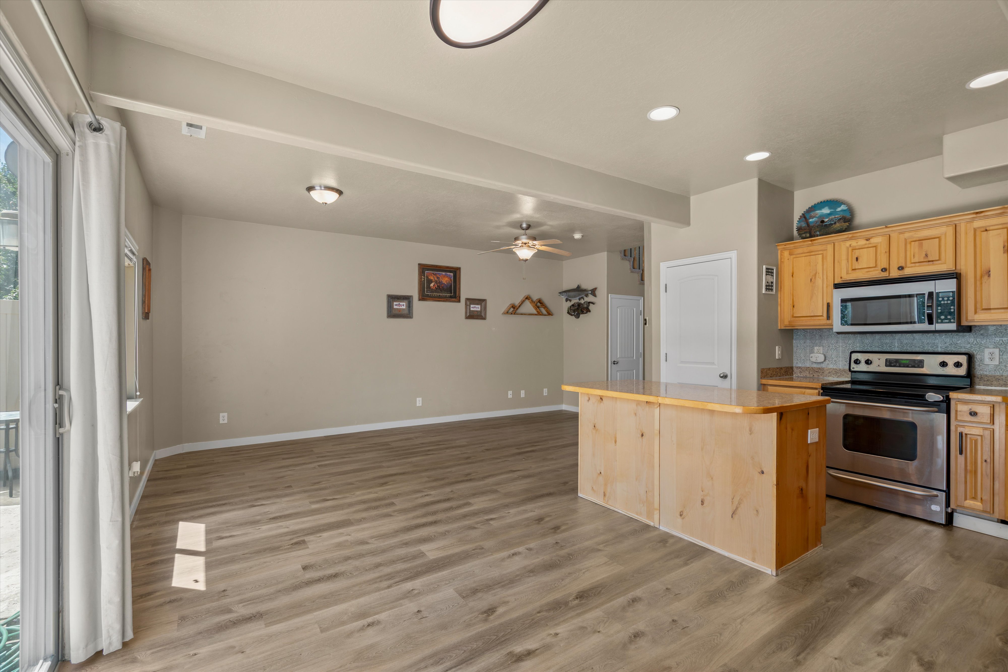 Open-concept living space featuring wood-finish flooring, a kitchen island with countertop, and stainless steel appliances including a range and microwave