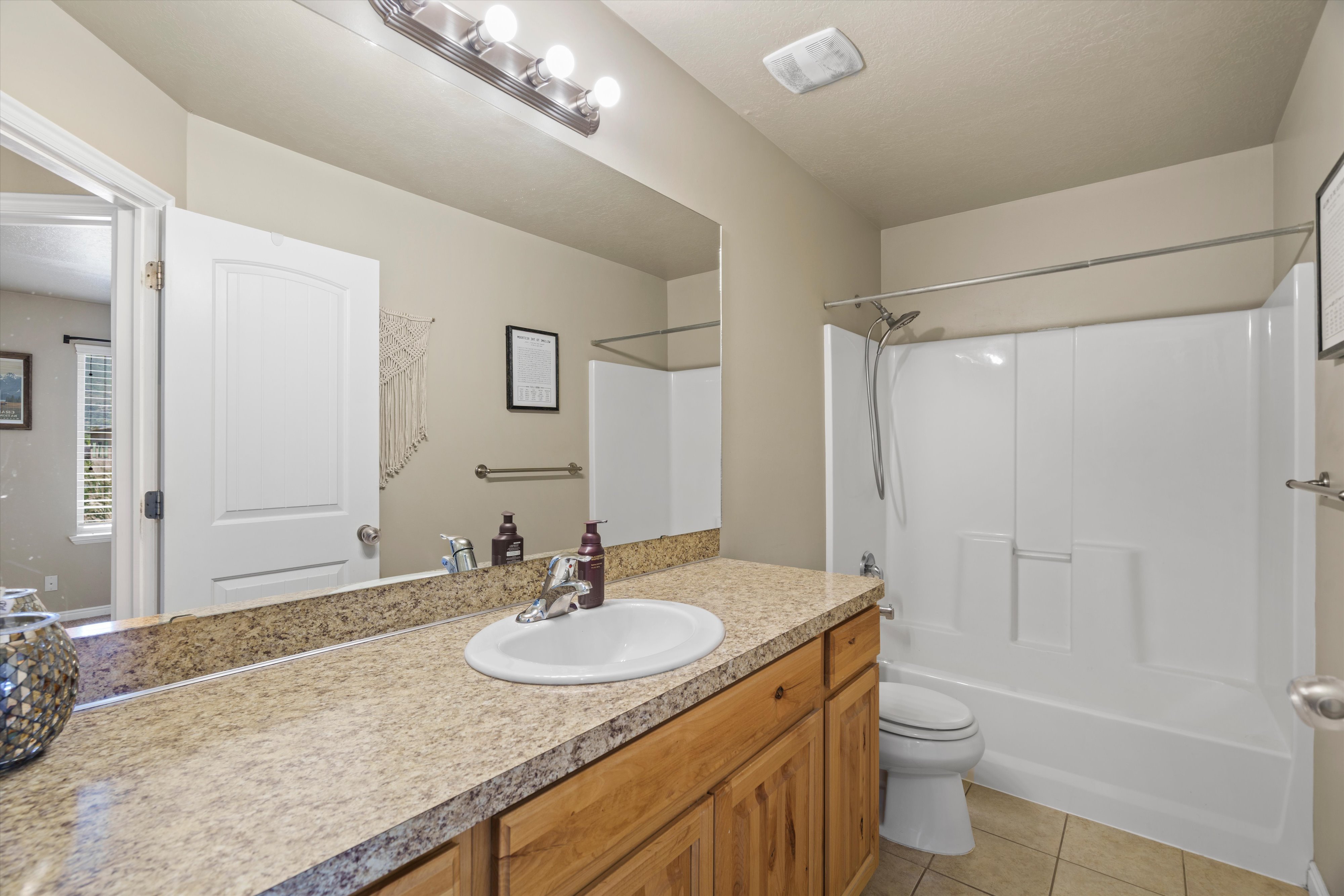 Full bathroom featuring a single vanity with a solid surface countertop, an undermount sink, and wood-finish cabinetry