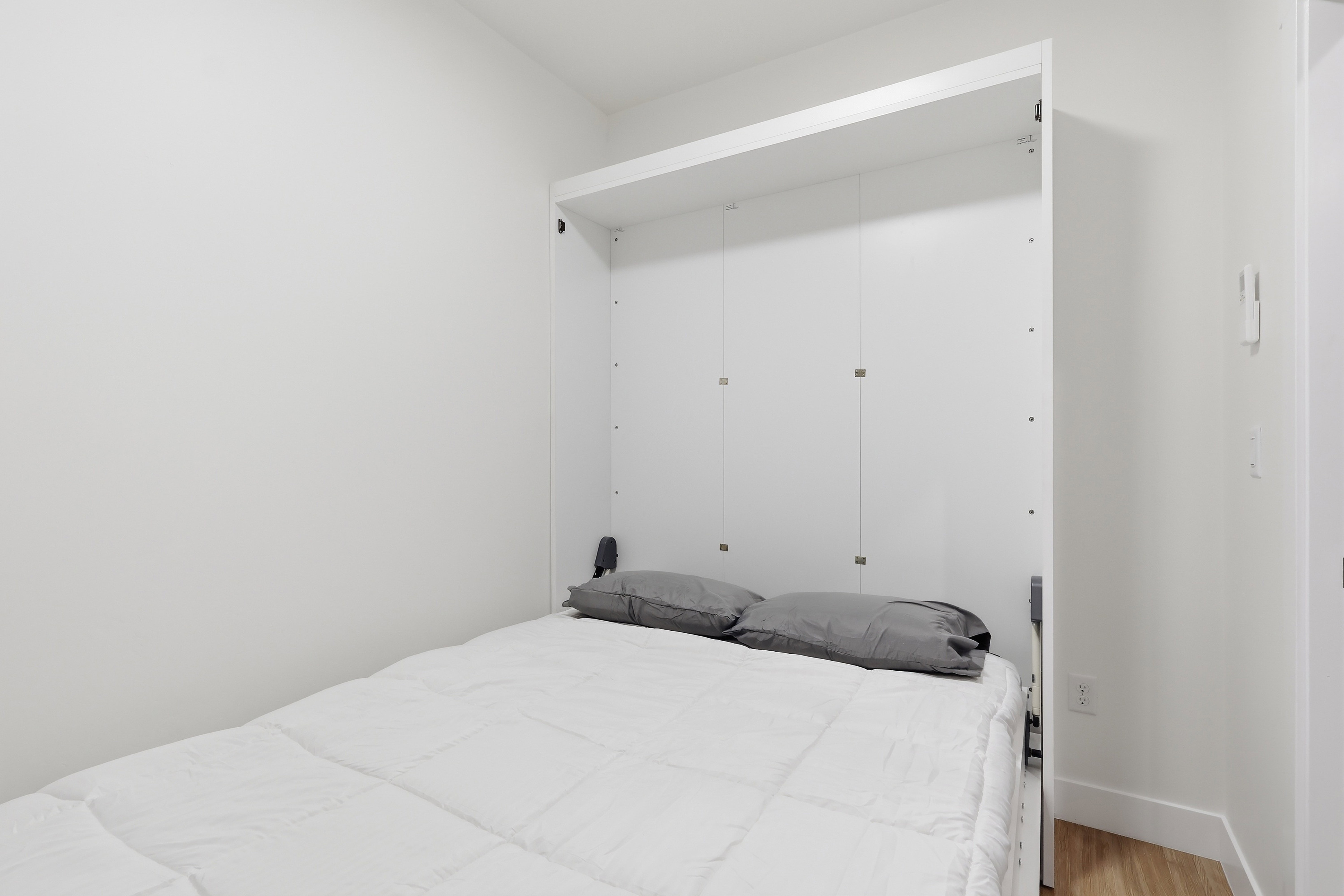 Integrated white wall bed with a light wood-finish flooring