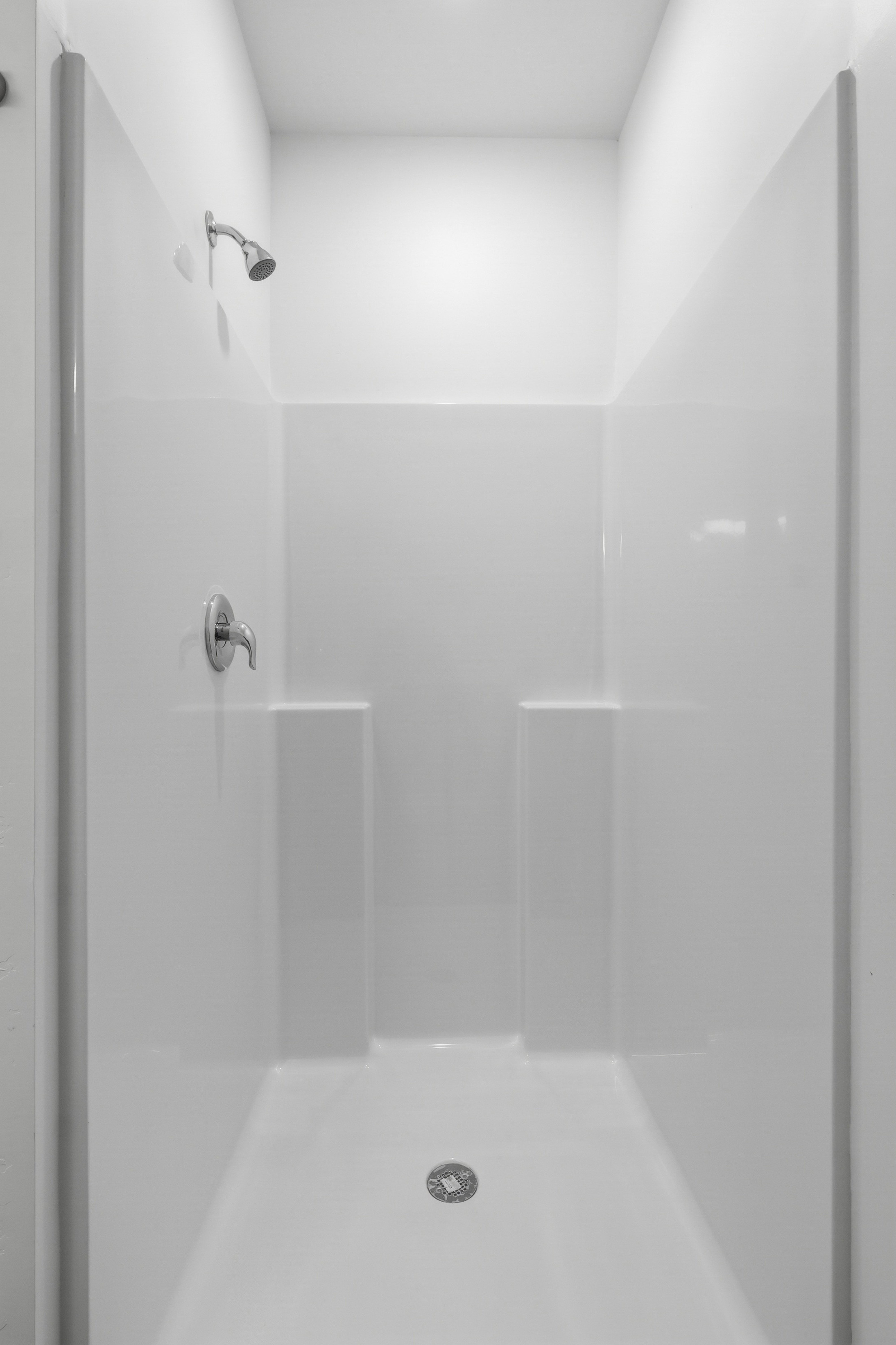 White shower enclosure with integrated shelving, chrome fixtures, and a ceiling-mounted showerhead