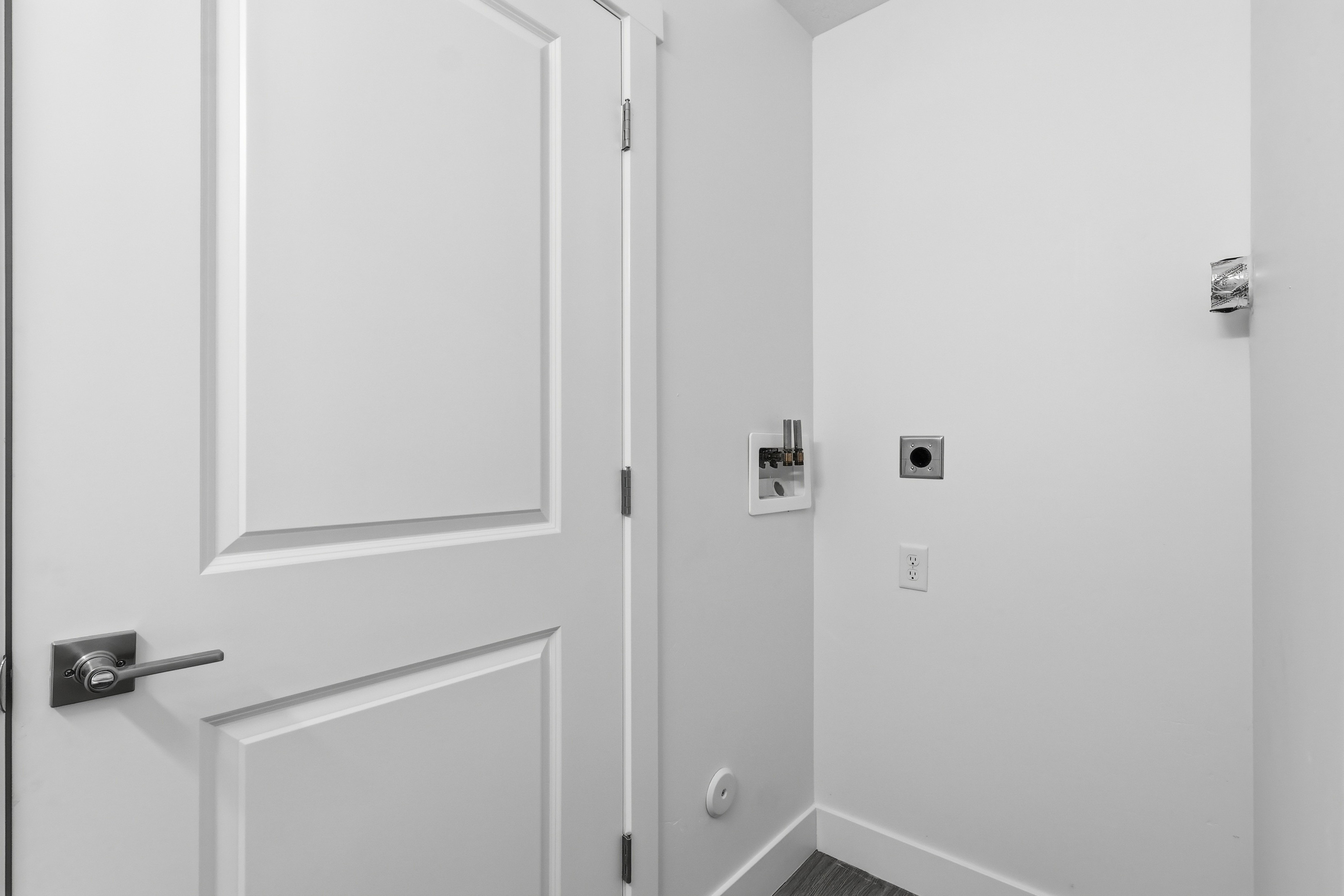 Utility area featuring a paneled door with brushed nickel hardware, a white laundry hookup box, a dryer vent, and electrical outlets