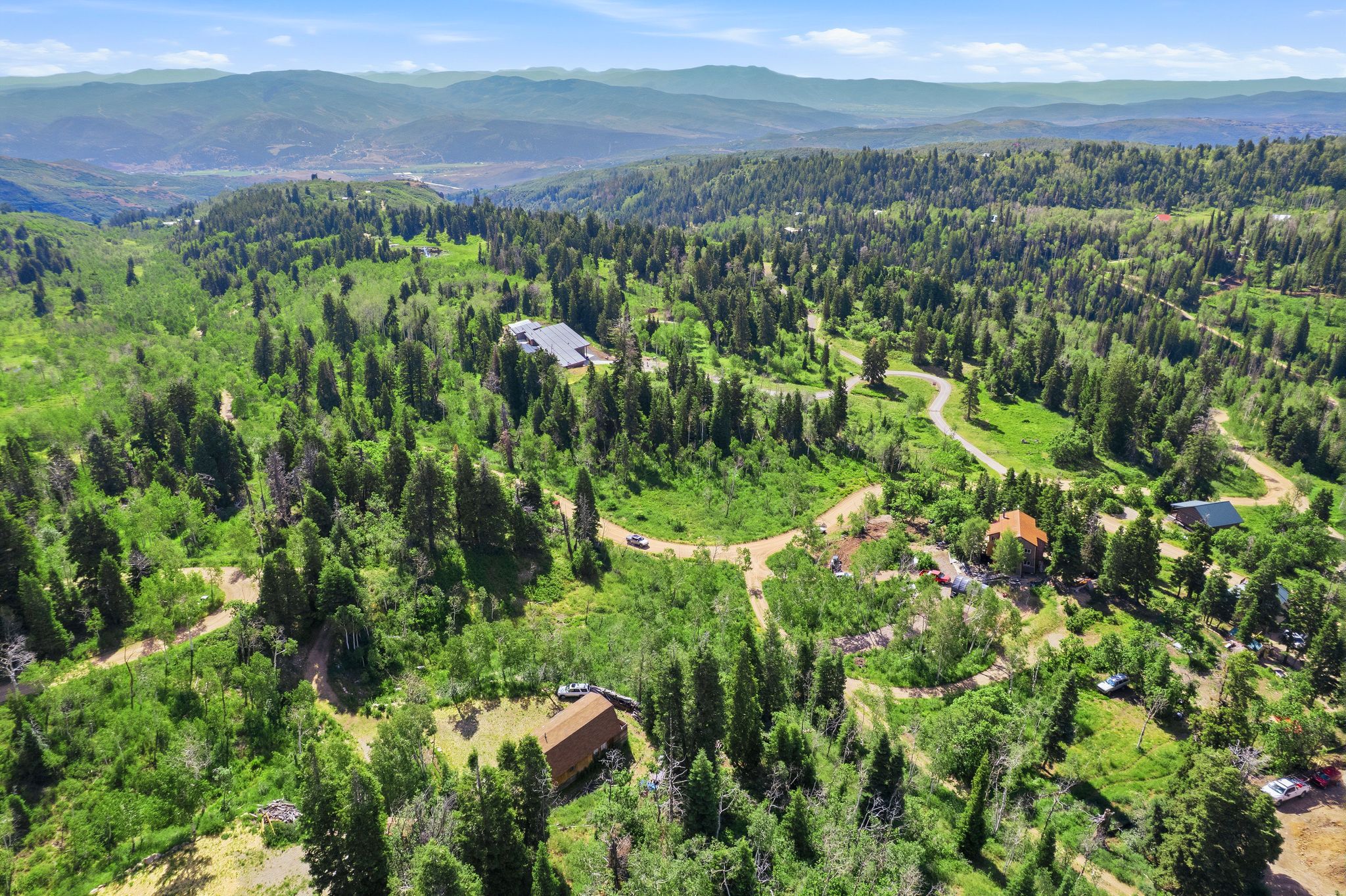 Expansive wooded terrain featuring multiple structures, winding pathways, and distant mountain ranges